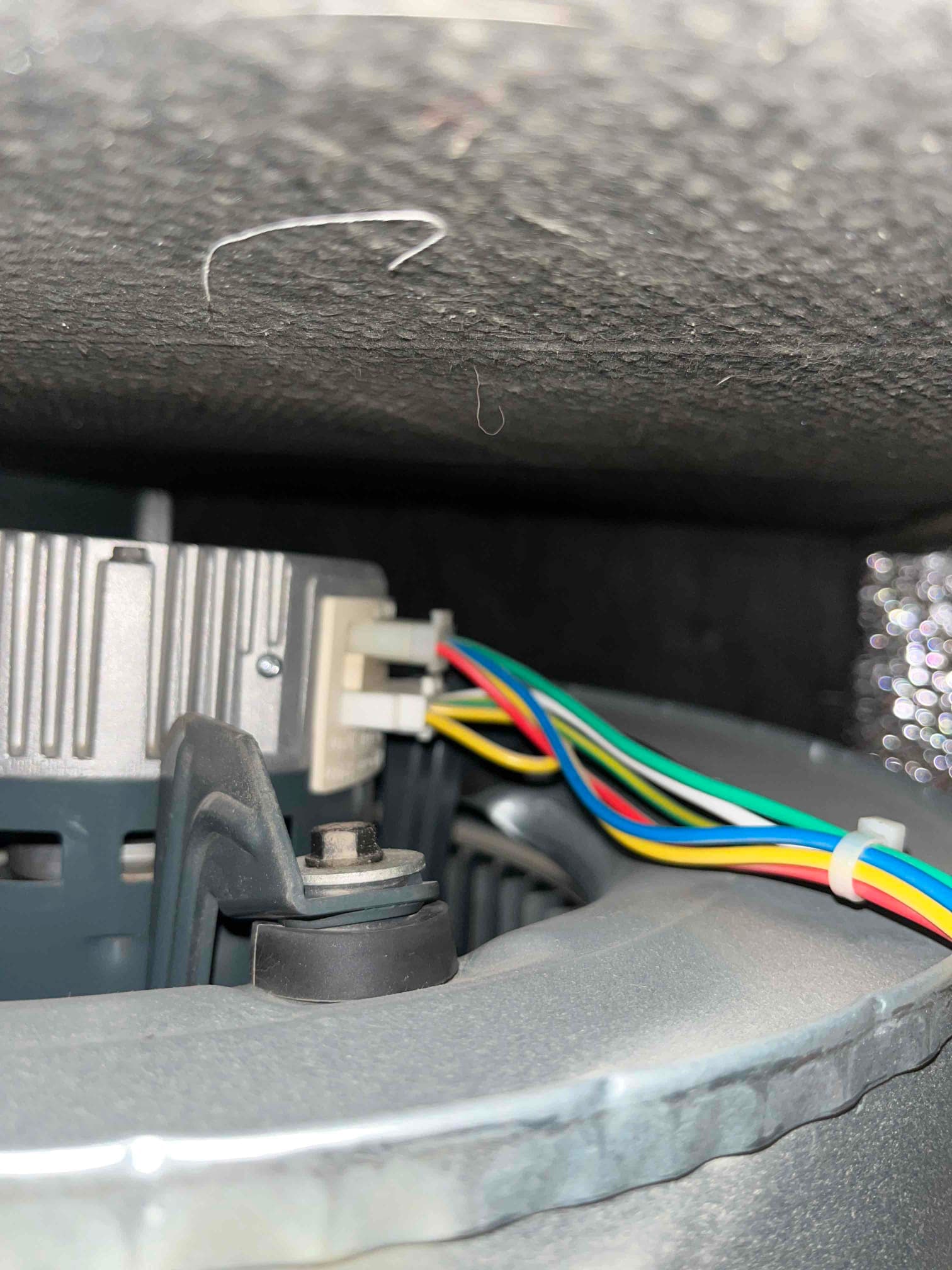 Blower motor and mounting bracket with multicolor wiring harness routed across the housing inside the air handler compartment.