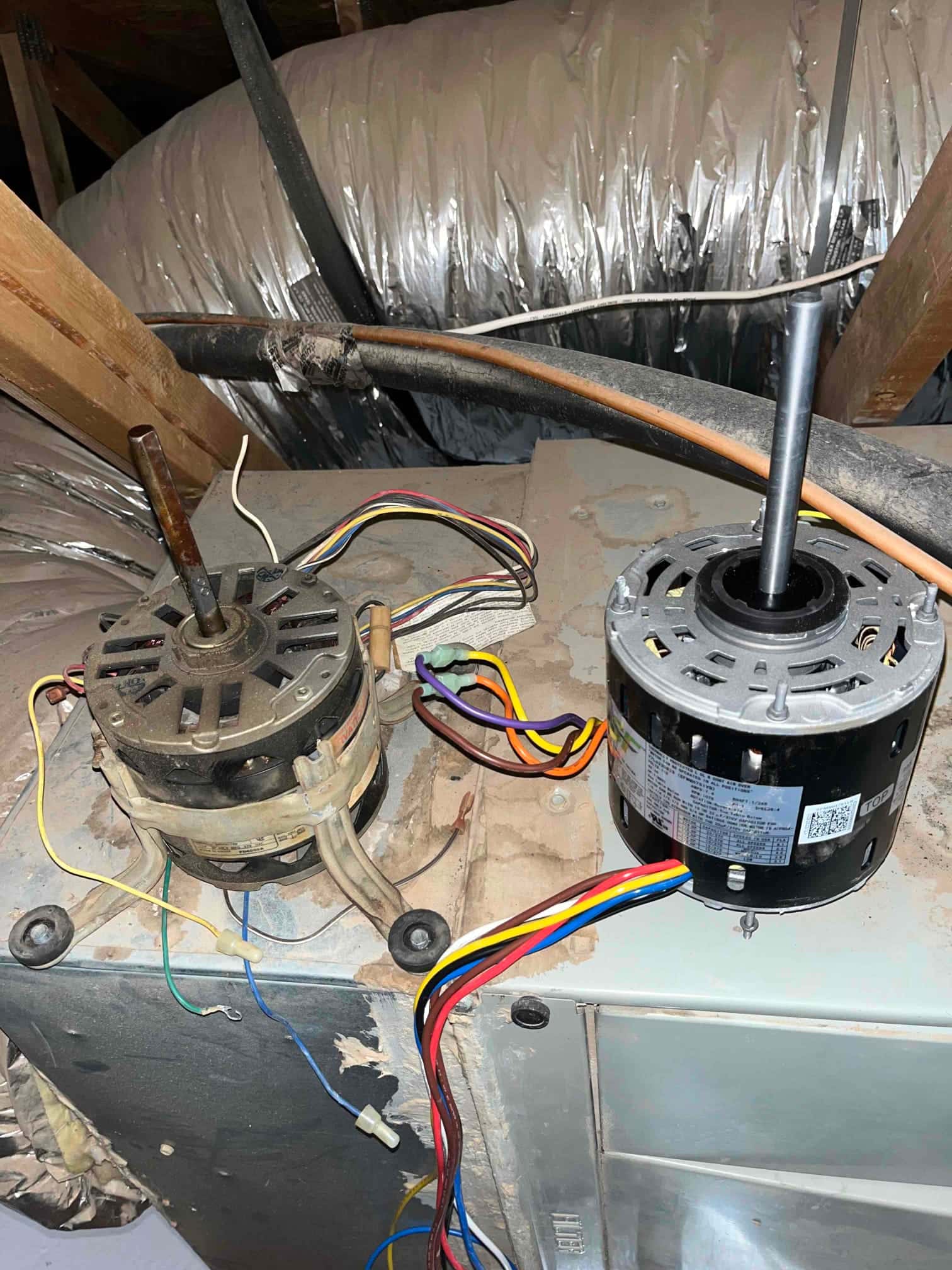 Two blower motors sit on the air handler, one dusty with mounting legs, one clean with color-coded wiring leads.