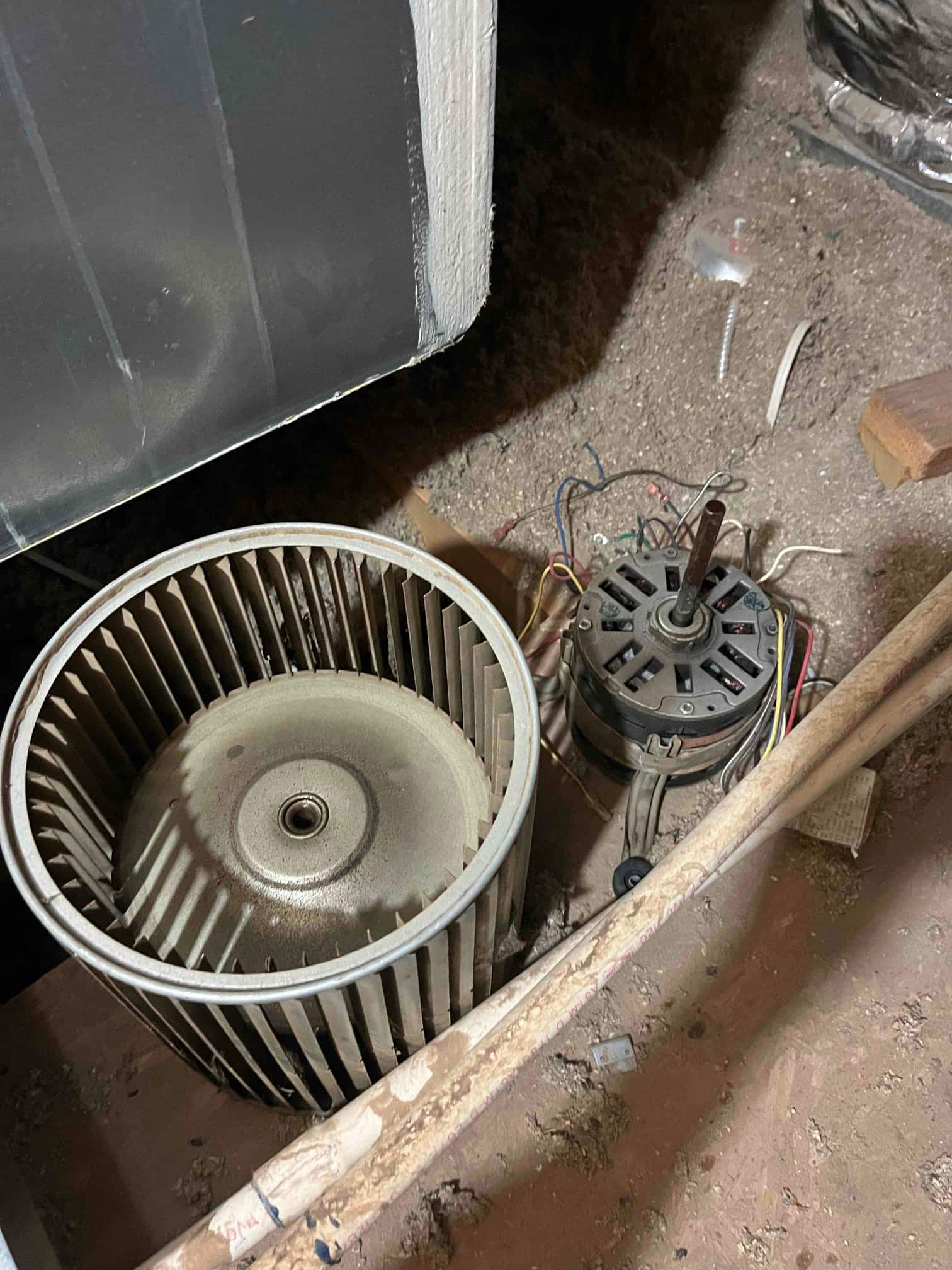 Blower wheel and motor sit on the floor beside the air handler cabinet, with wiring and dust visible.