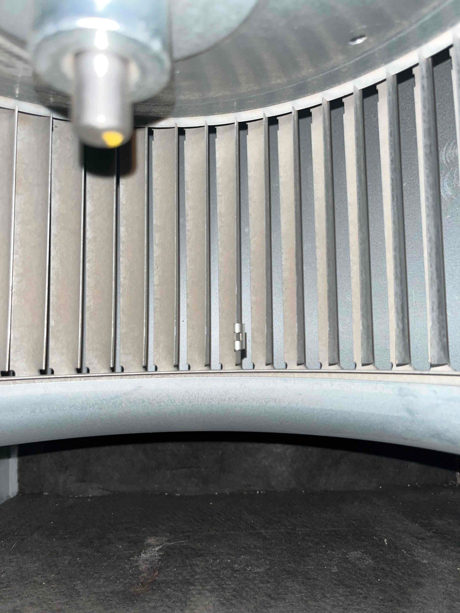Centrifugal blower wheel inside the air handler housing, showing straight fins and a small balancing clip on one blade.