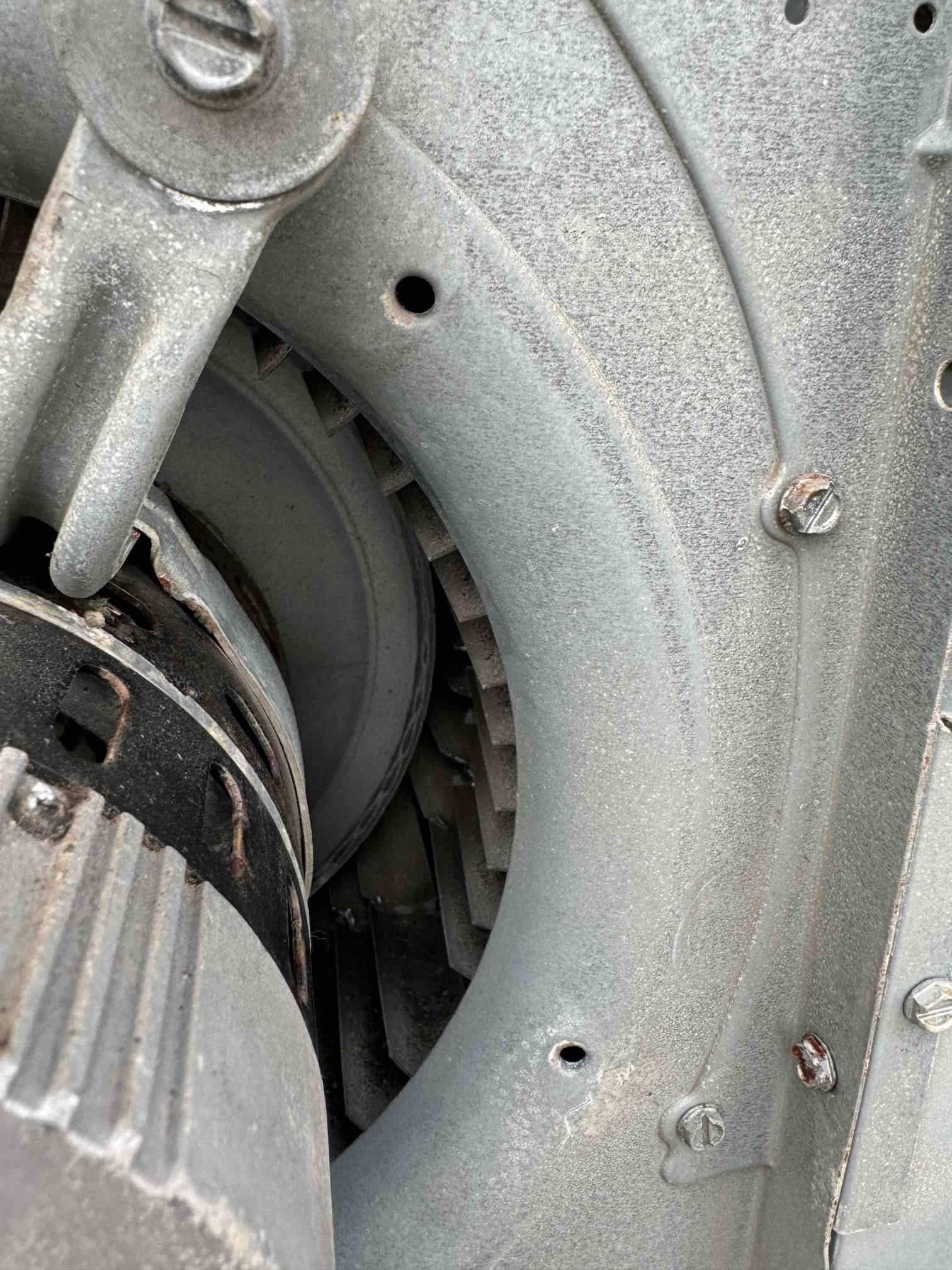 Close-up of a blower wheel and motor inside the metal housing, with dust buildup and visible mounting screws.
