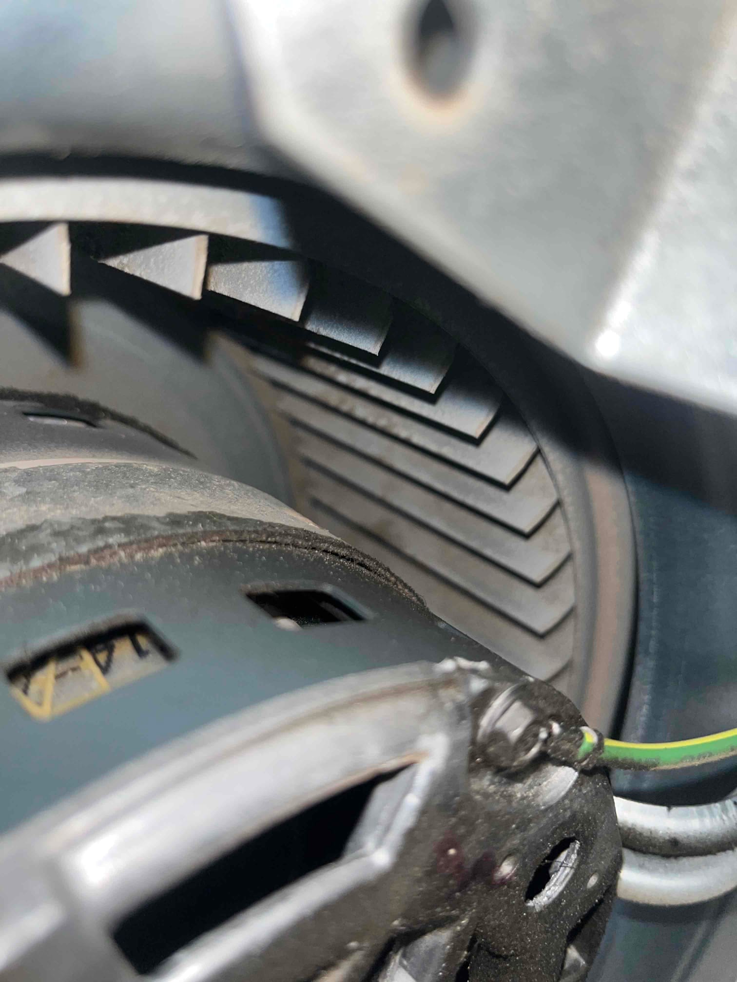 Close-up of a centrifugal blower wheel and adjacent motor housing with a green ground wire visible inside the HVAC assembly.