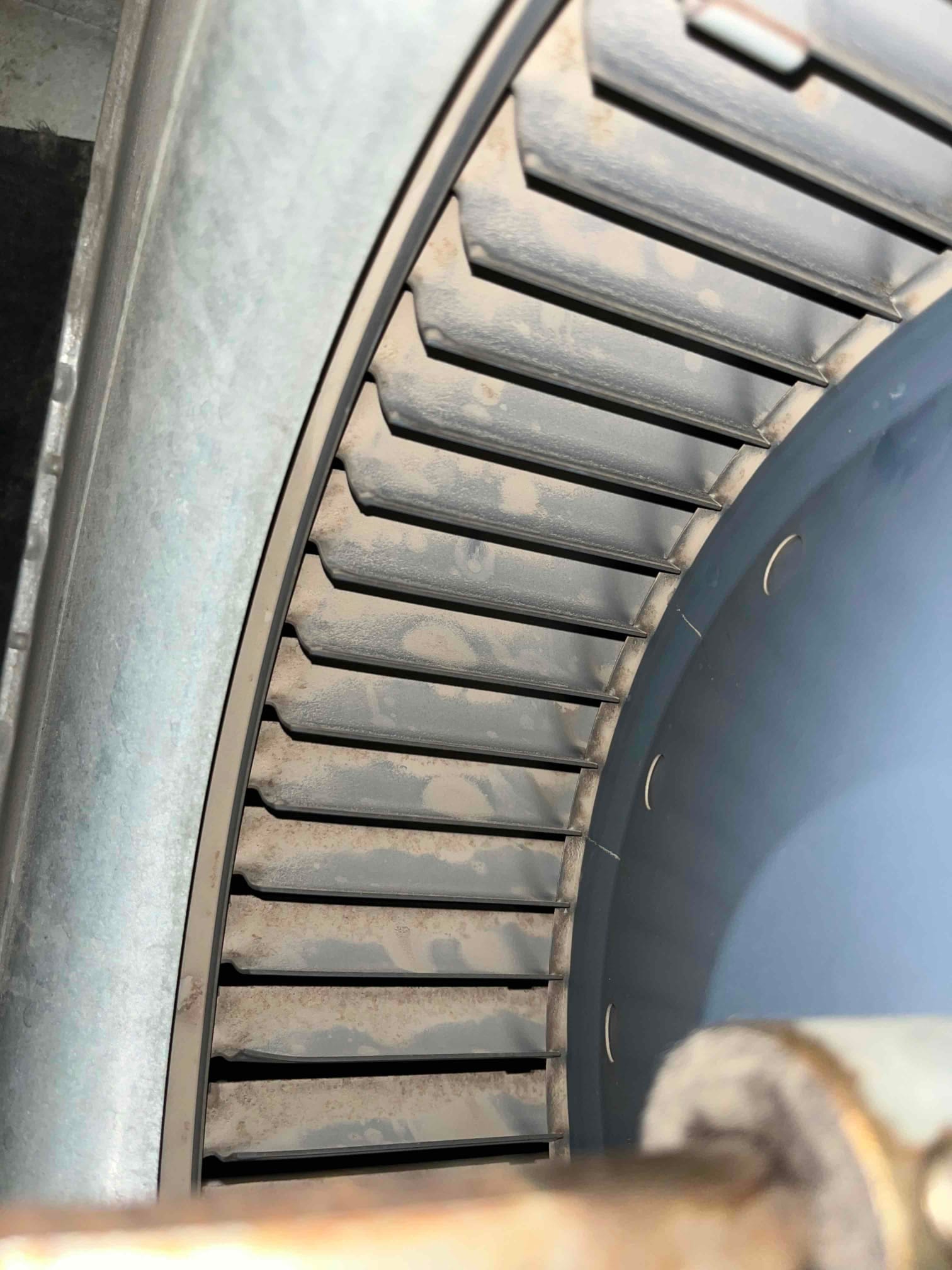 Close-up of an HVAC blower wheel showing accumulated dust on the fins inside the housing.