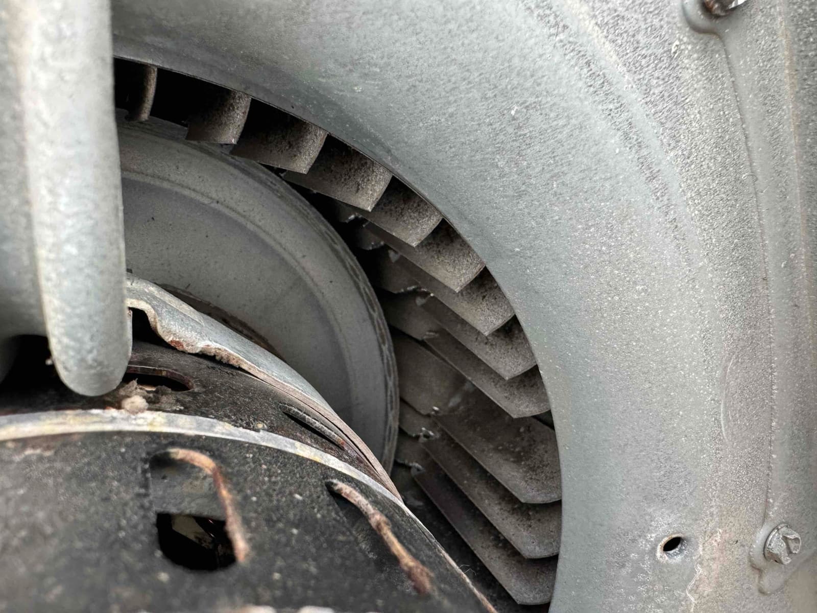 Close-up of an indoor blower wheel and housing with accumulated dust on fins and surface rust on the motor housing.