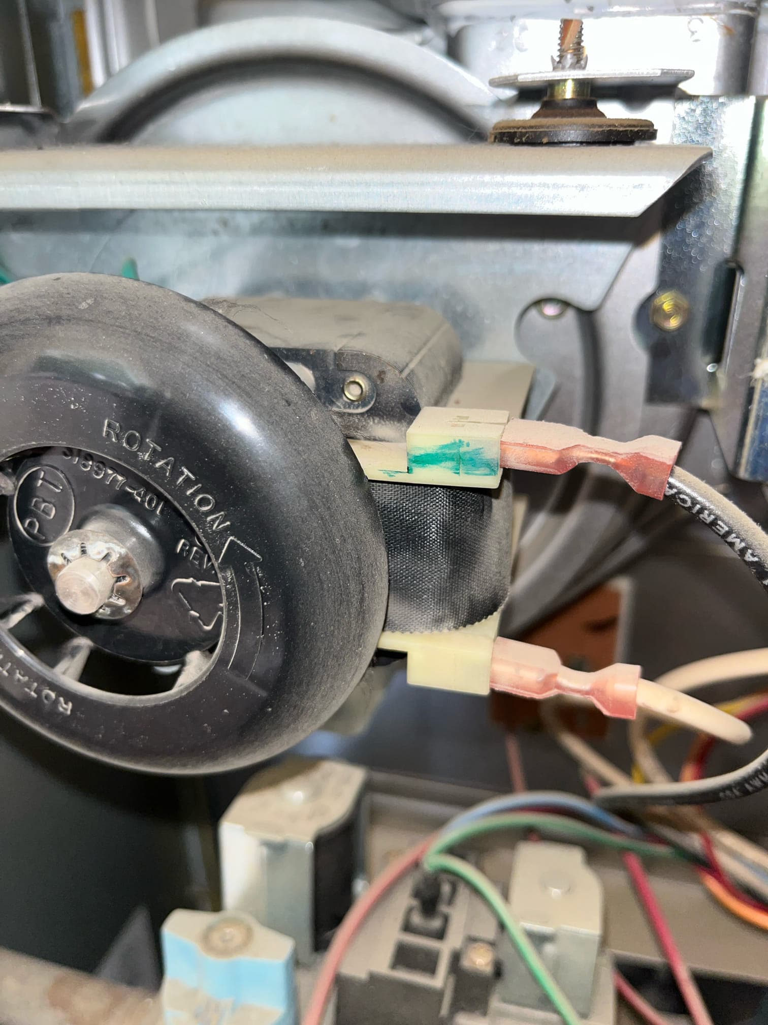 Close-up inside a furnace shows a black rotating wheel, two spade-connected switch terminals, and surrounding wiring and metal housing.