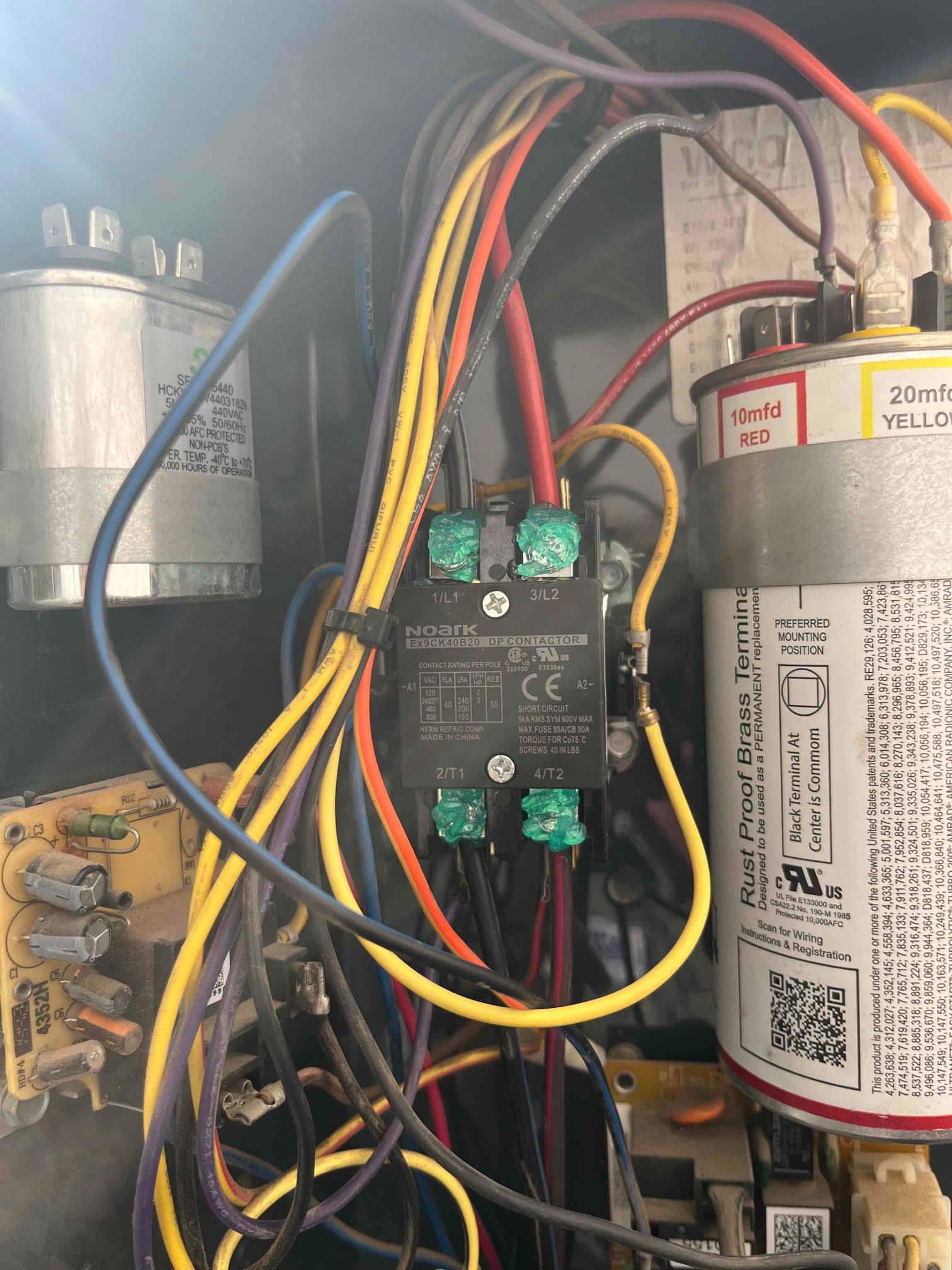 Contactor with connected wiring inside condenser compartment, with capacitors on both sides; right capacitor label states 10 mfd RED and 20 mfd YELLOW.