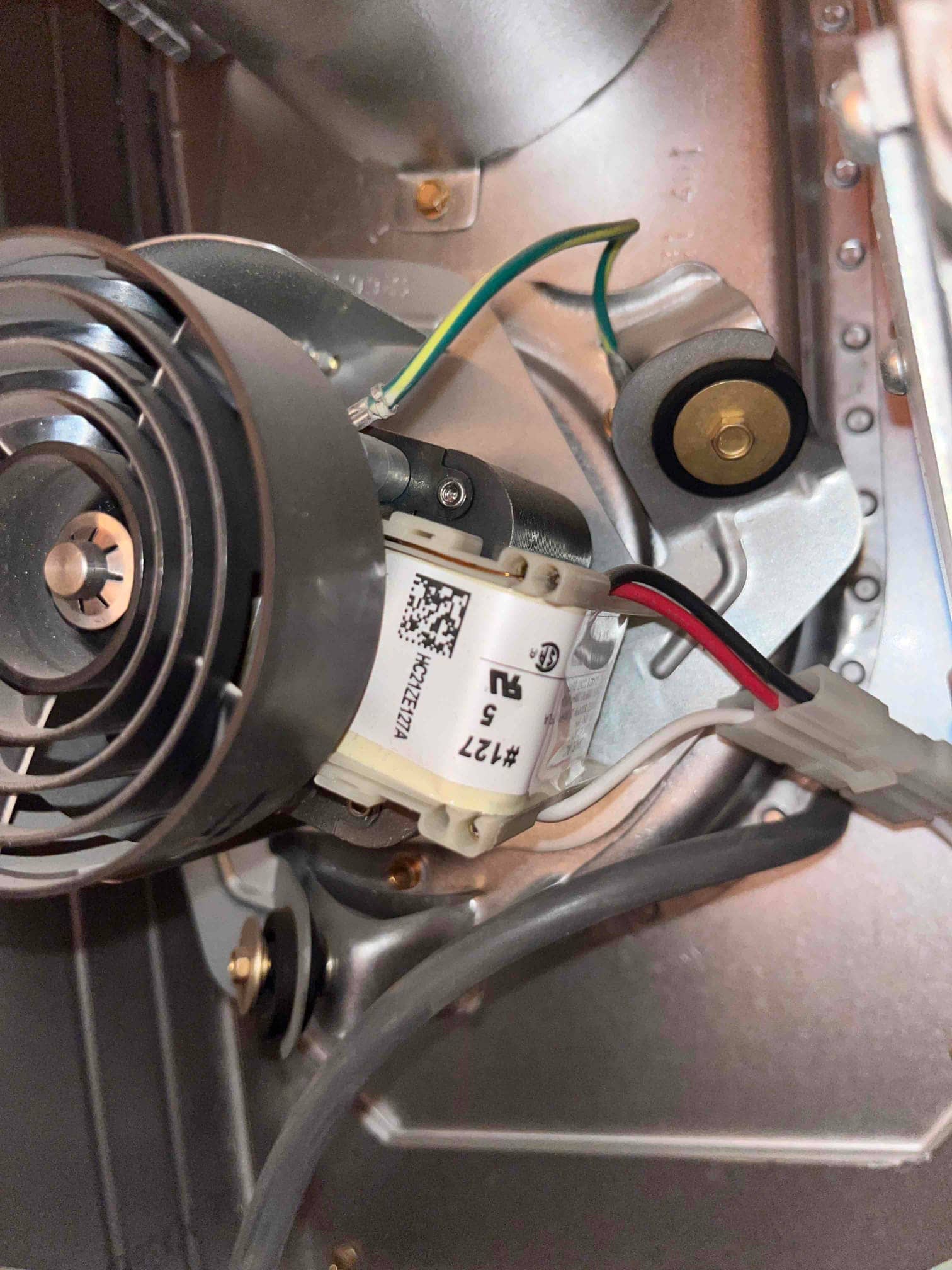 Draft inducer motor assembly inside a furnace, showing wiring connections, ground lead, rubber mounts, and blower wheel.