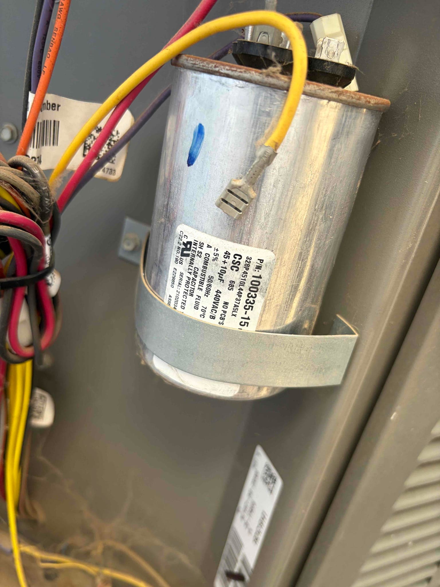 Dual-run capacitor labeled 45/5 μF with connected wiring and mounting strap inside the outdoor unit cabinet.