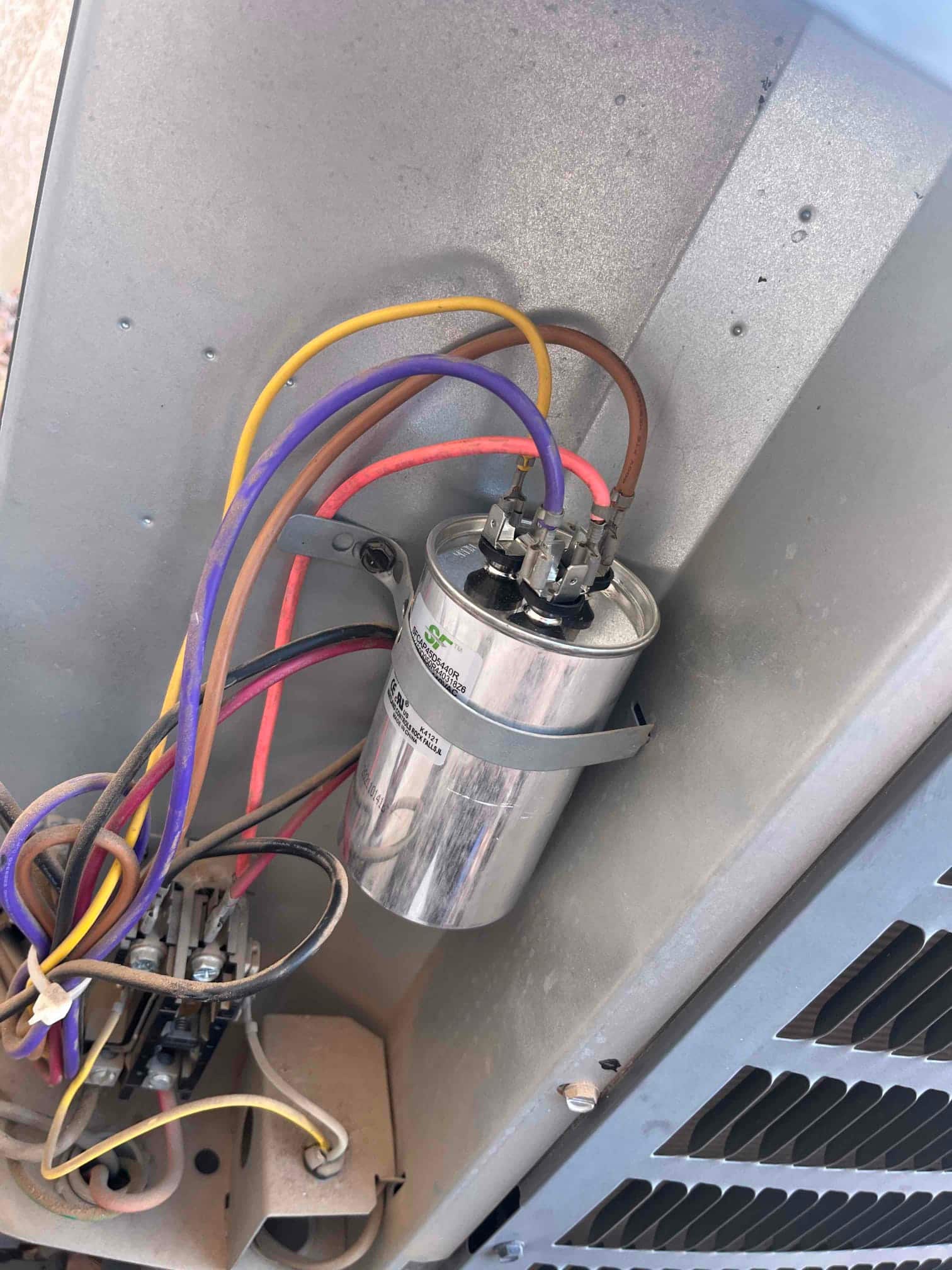 Dual-run capacitor mounted in condenser control panel with multiple colored wires connected and contactor assembly below.