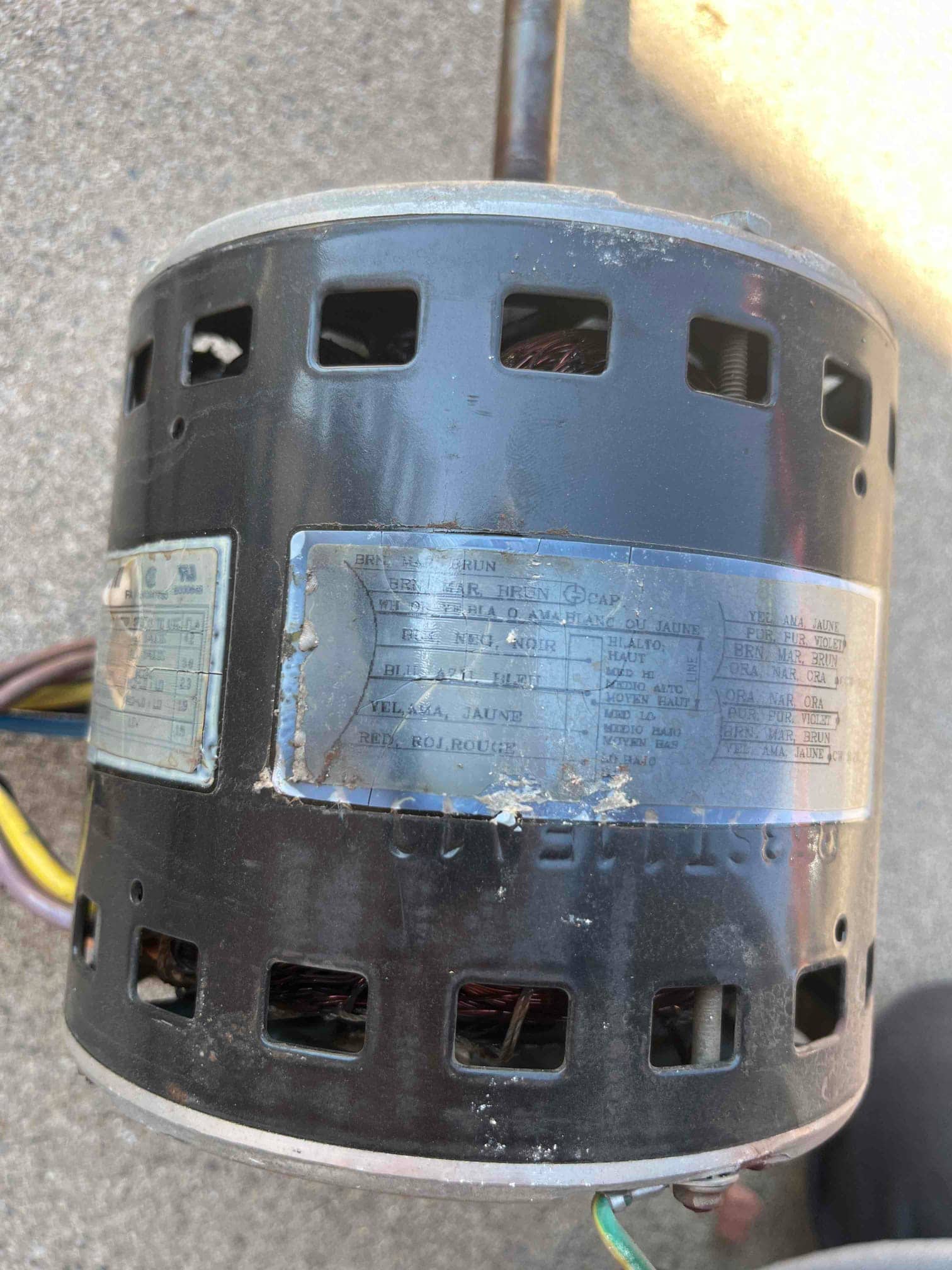 Electric motor removed, showing ventilation openings, copper windings inside, multiple color-coded wires, and a worn specification label.