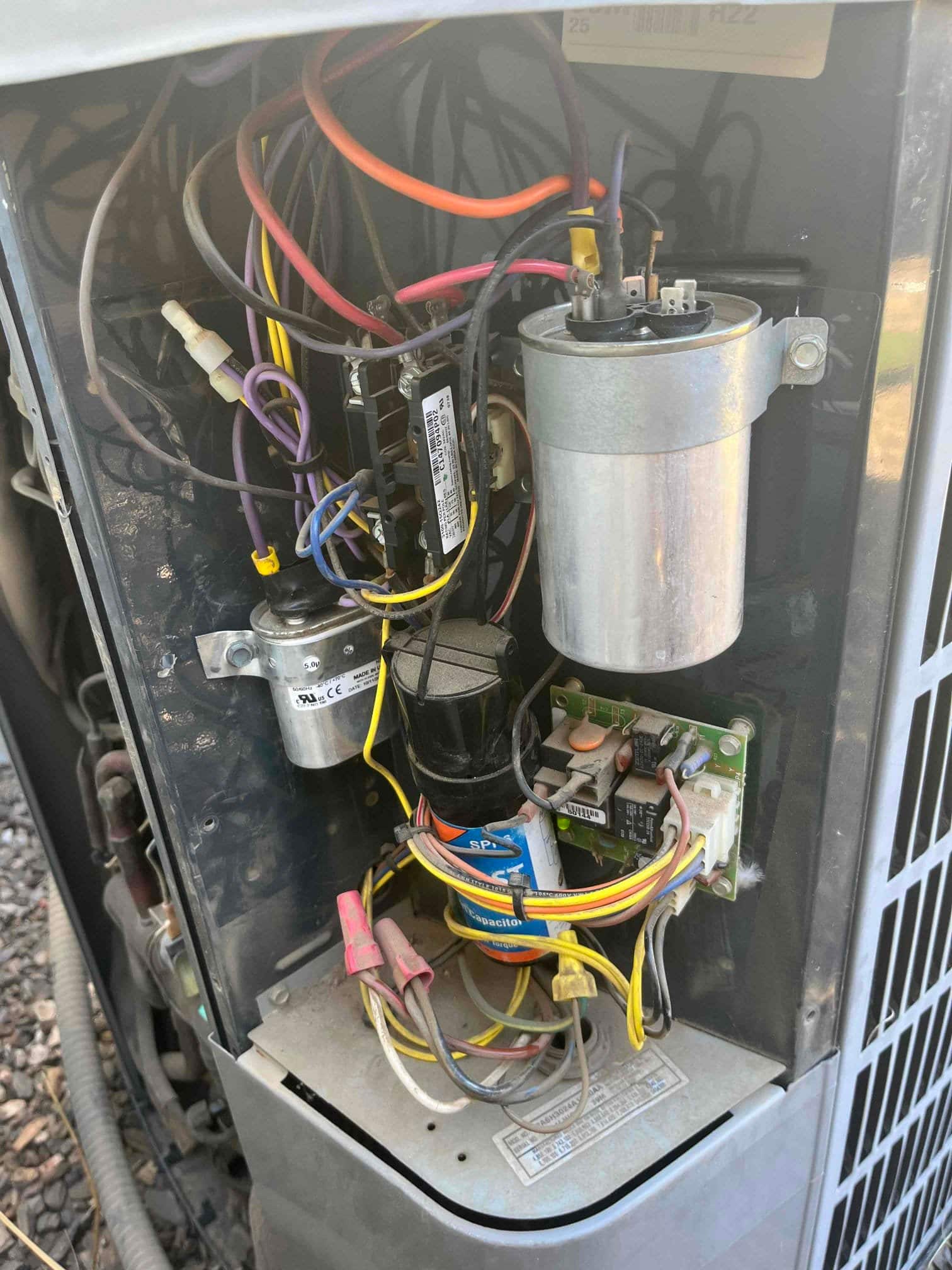 Electrical compartment of an outdoor condenser showing capacitors, contactor, control board, and multiple connected wires and wire nuts.