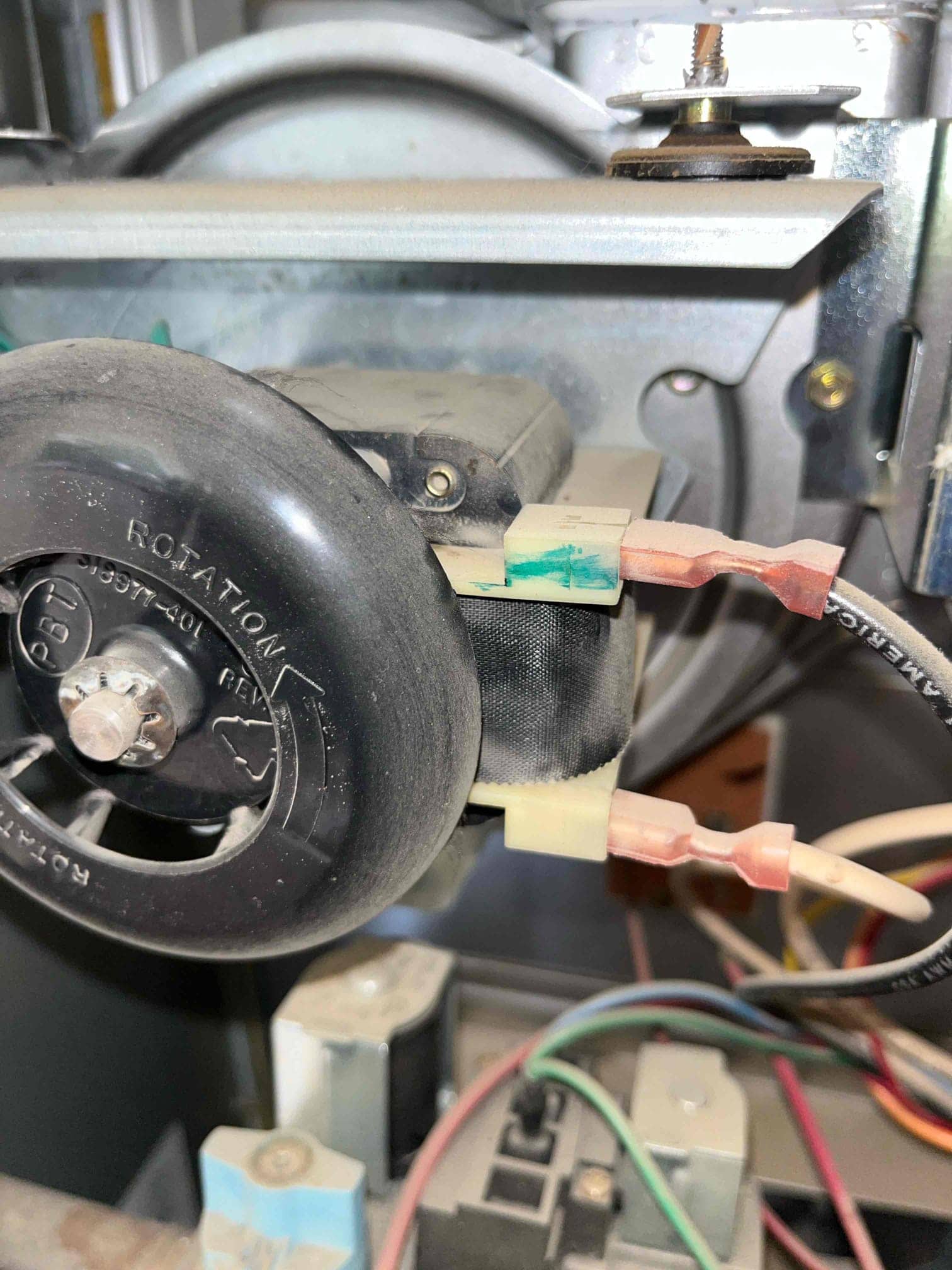 Electrical spade connectors and wiring on a small motor with a rotation-labeled wheel inside the furnace cabinet.