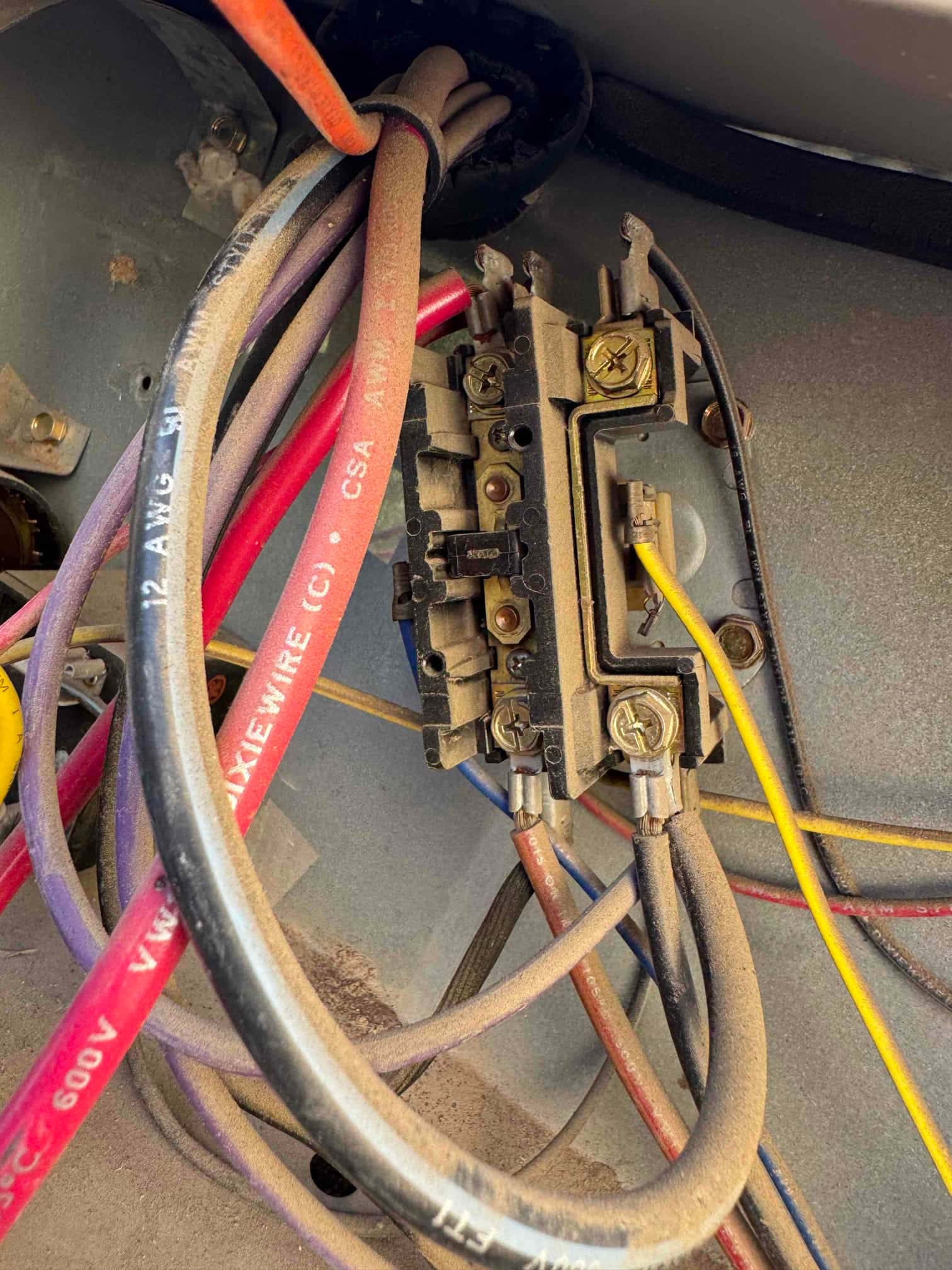 Electrical terminals and multiple colored wires inside an HVAC unit control compartment, with dust visible on the components and cable insulation.