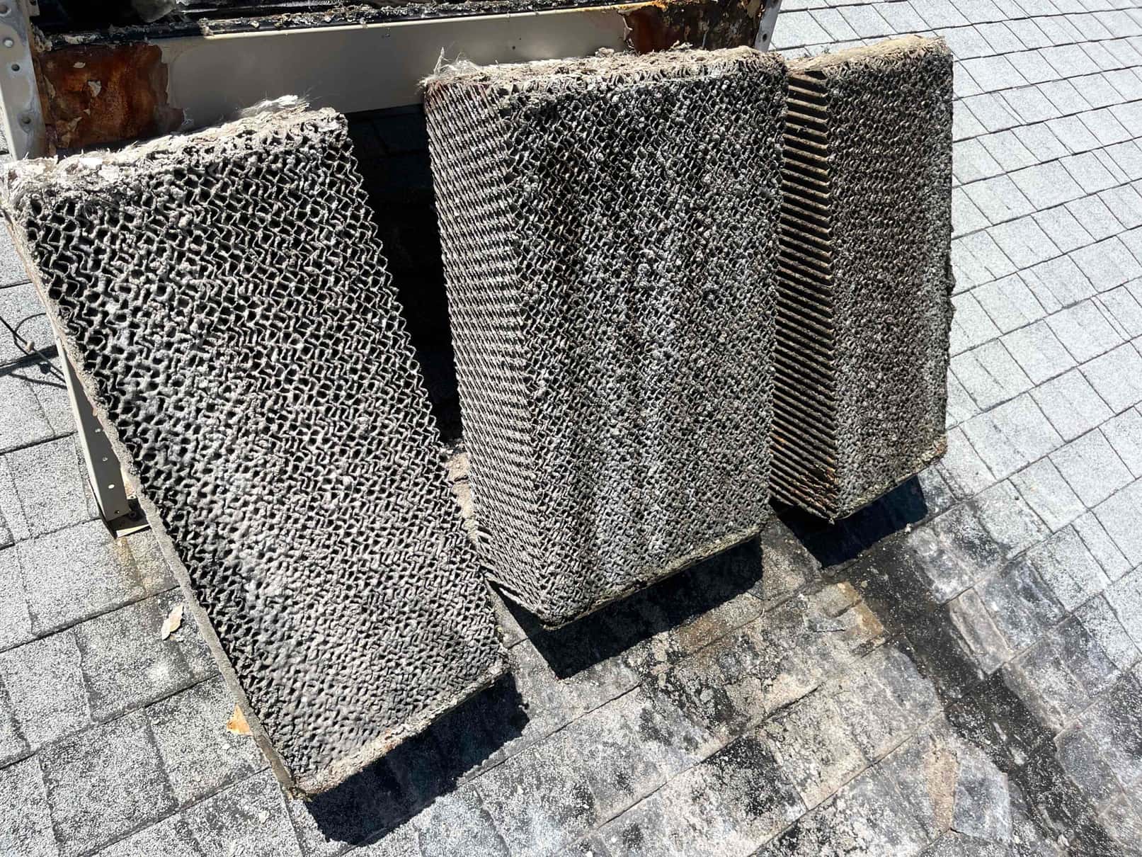 Three evaporative cooler pads removed on a rooftop, showing heavy mineral deposits and debris across the pad surfaces.