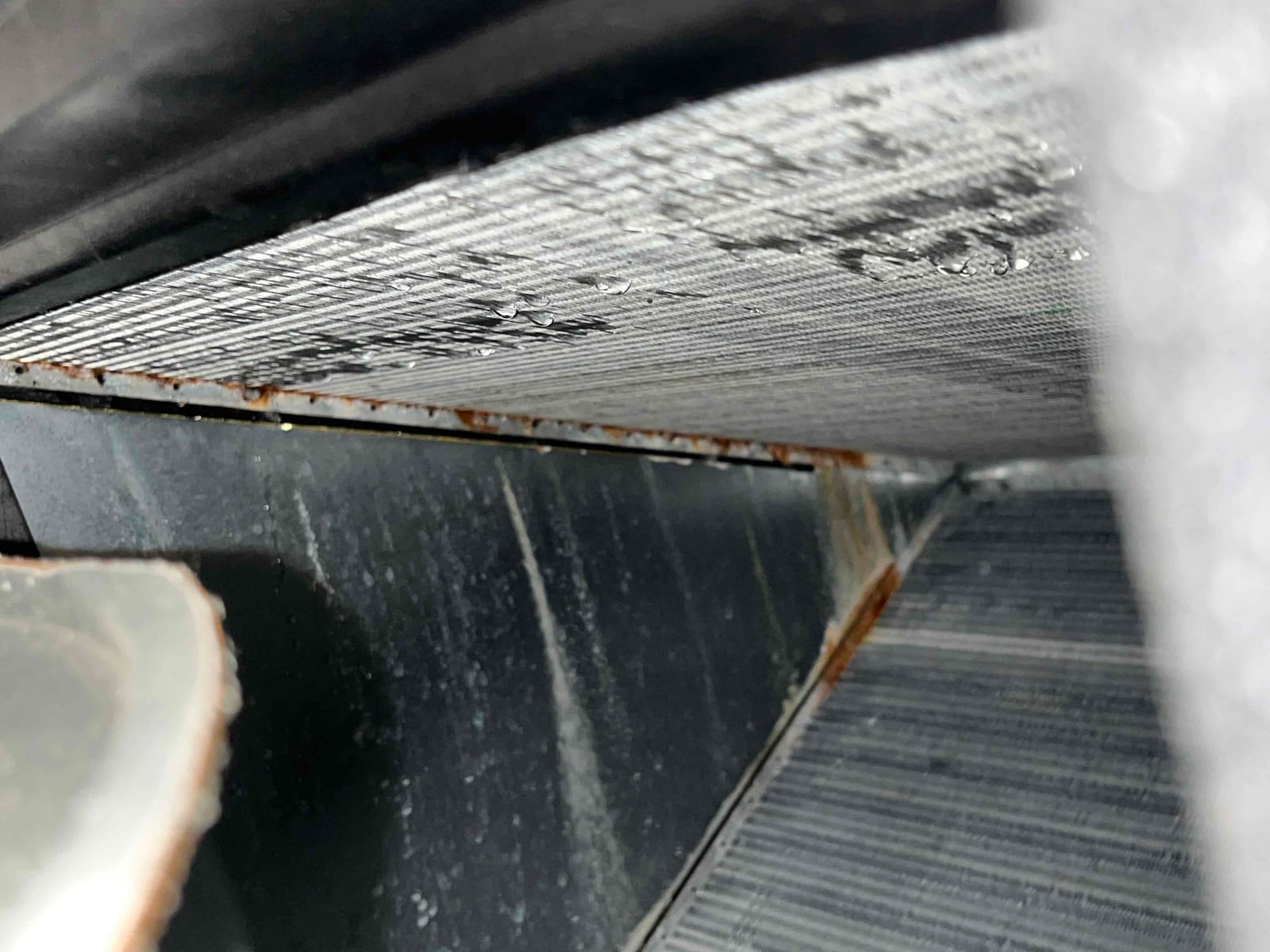 Evaporator coil fins with water droplets and visible rust along the metal frame inside housing.
