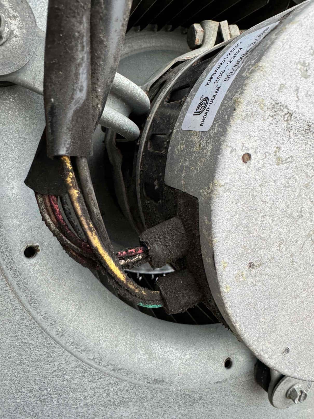 Fan motor housing with wiring harness and protective sleeve, showing accumulated dust and surface wear around the assembly.