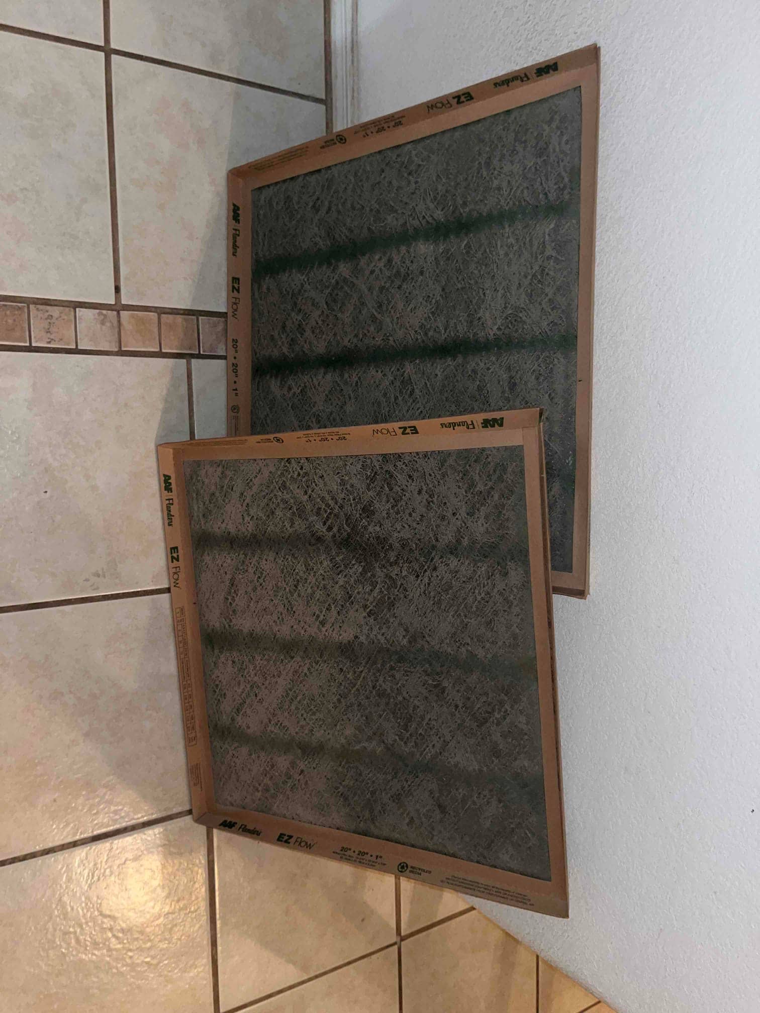 Two fibrous disposable air filters on tile floor, each labeled 20 x 20 x 1 in.