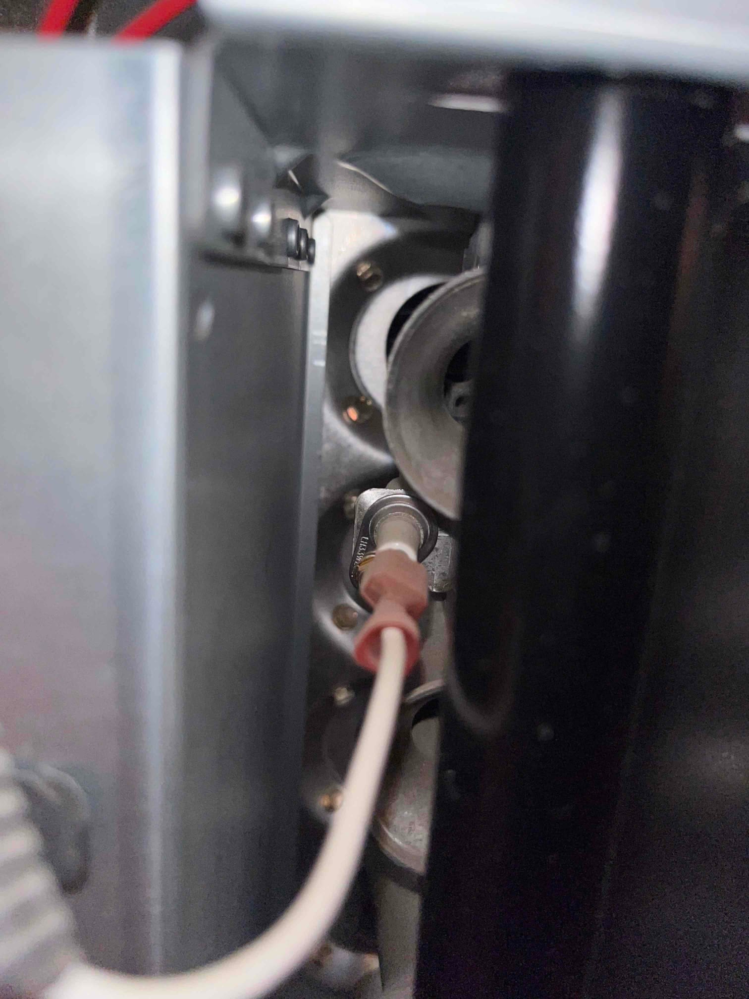 Flame sensor mounted at the burner assembly with white lead connected and surrounding metal housing.