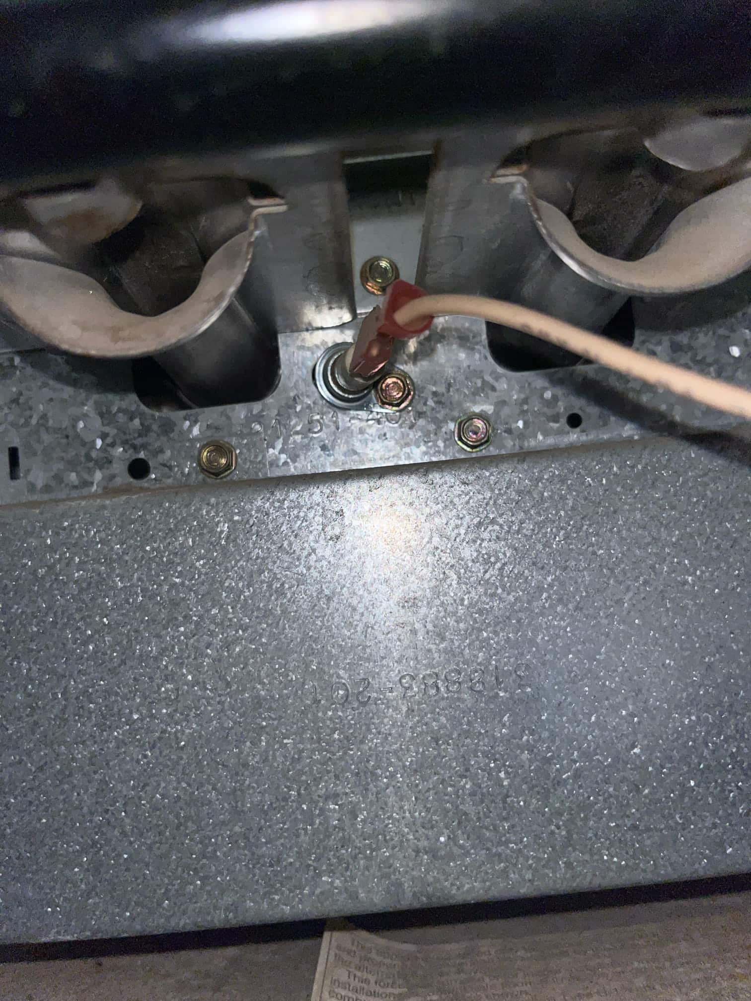 Flame sensor with red spade connector mounted in front of gas furnace burners.