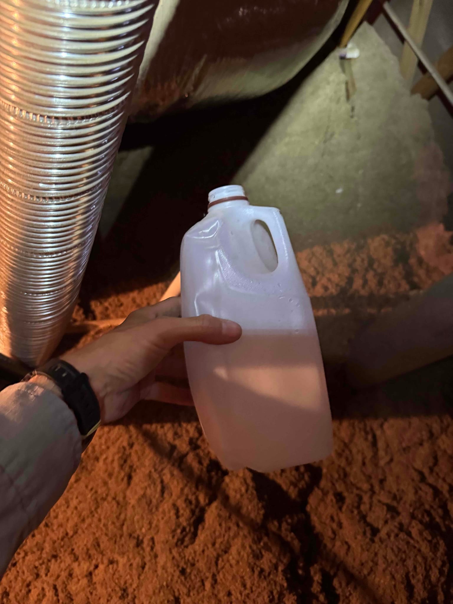 Flexible air duct and insulated trunk in attic; technician holds a plastic container nearby.