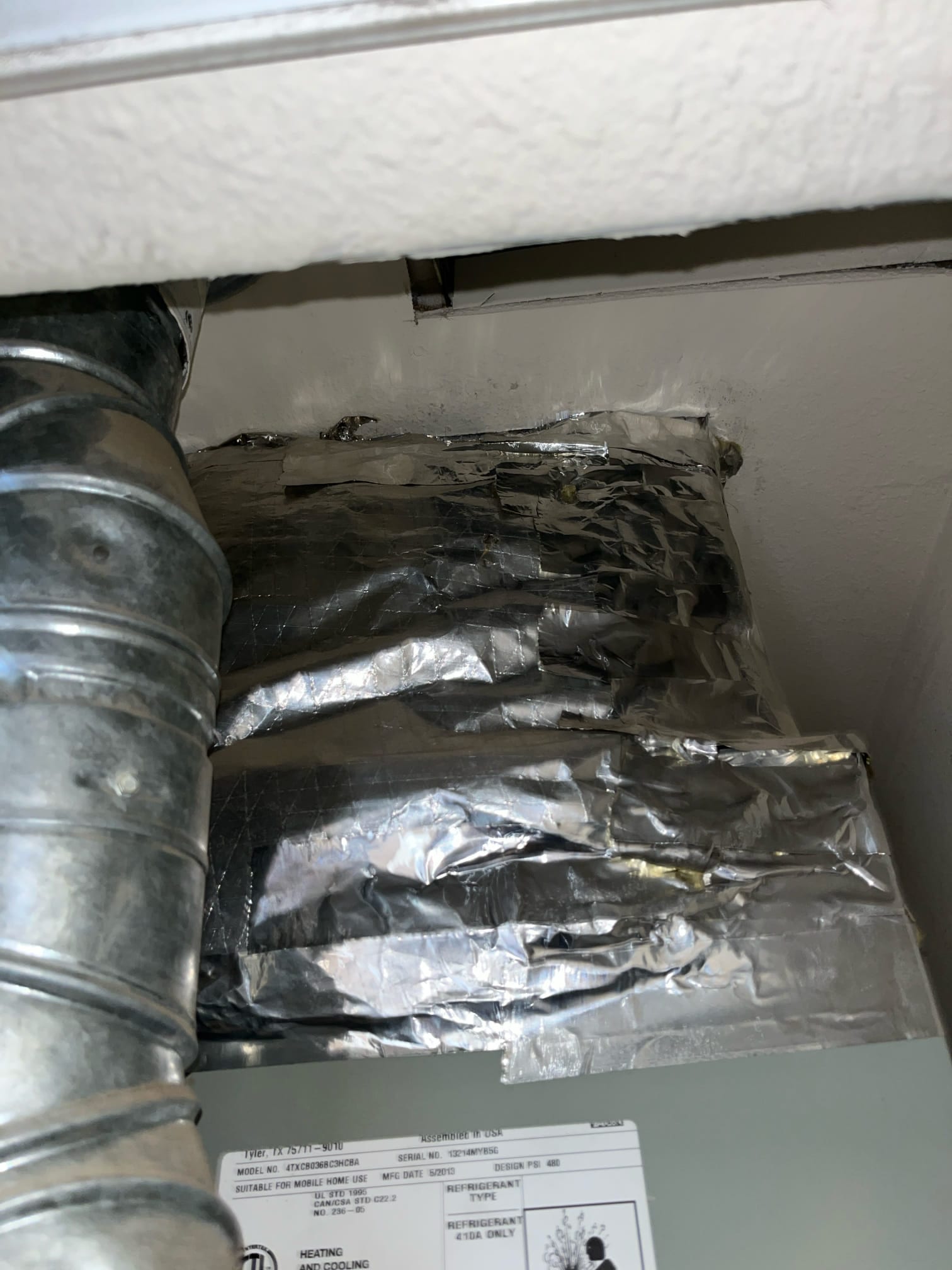 Foil-taped duct plenum above an indoor air handler, with a round metal duct on the left.