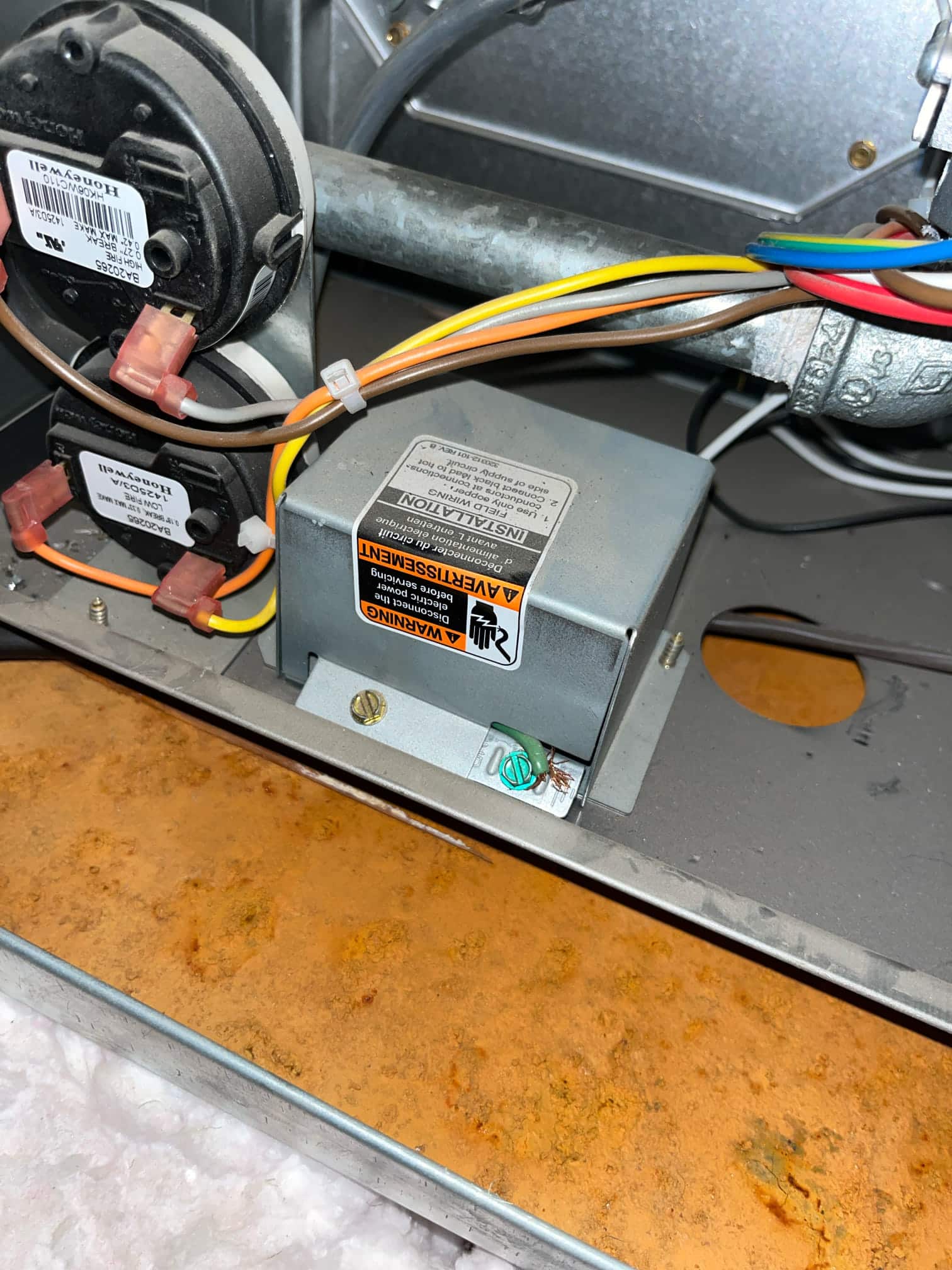 Furnace compartment shows two pressure switches with connected wiring and a gray electrical box above a rust-colored drain pan.