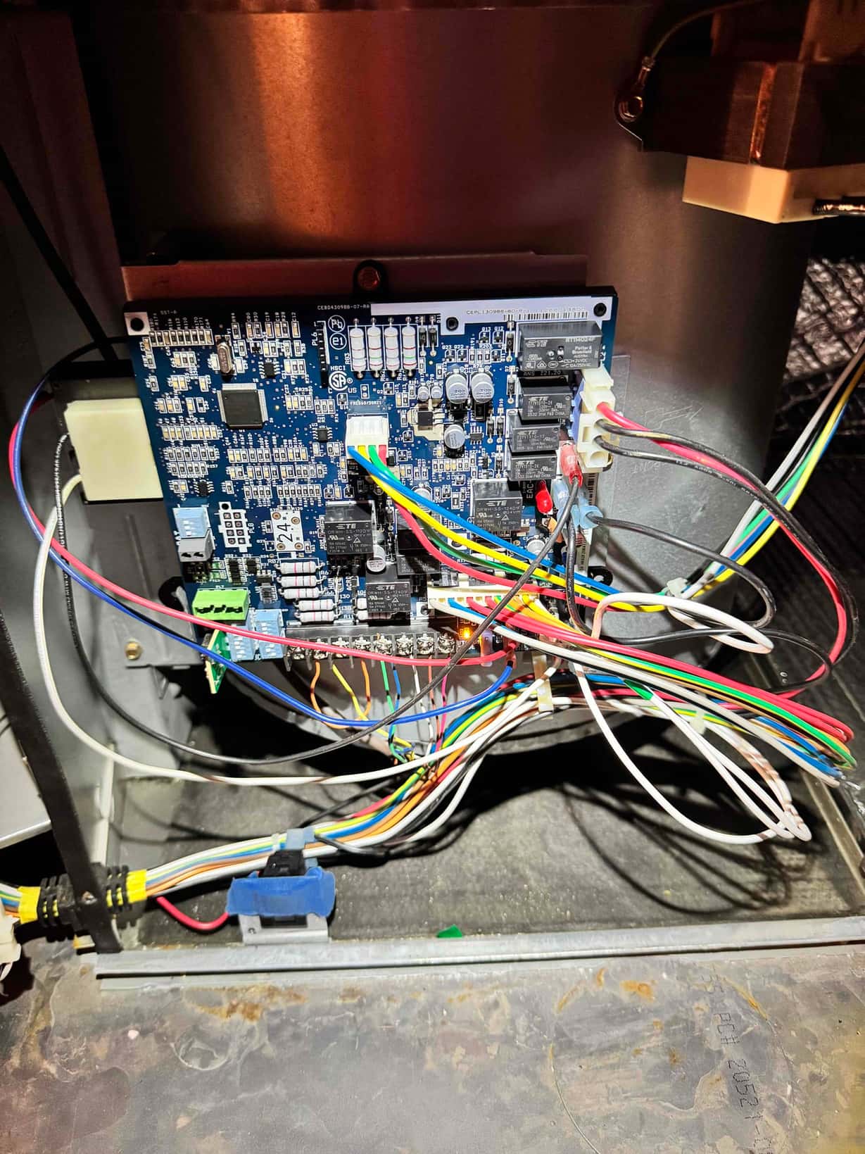 Furnace control board inside the air handler cabinet with multiple relays, connectors, and color-coded wiring harnesses attached.