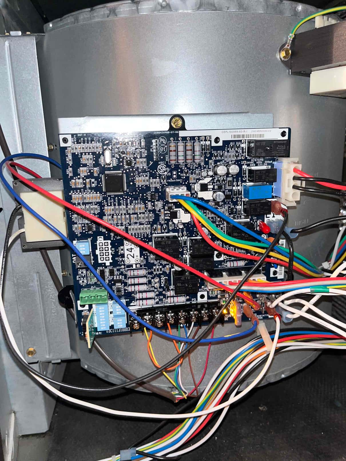 Furnace control board mounted in the blower compartment with multiple low-voltage and line-voltage wires connected and status LEDs illuminated.