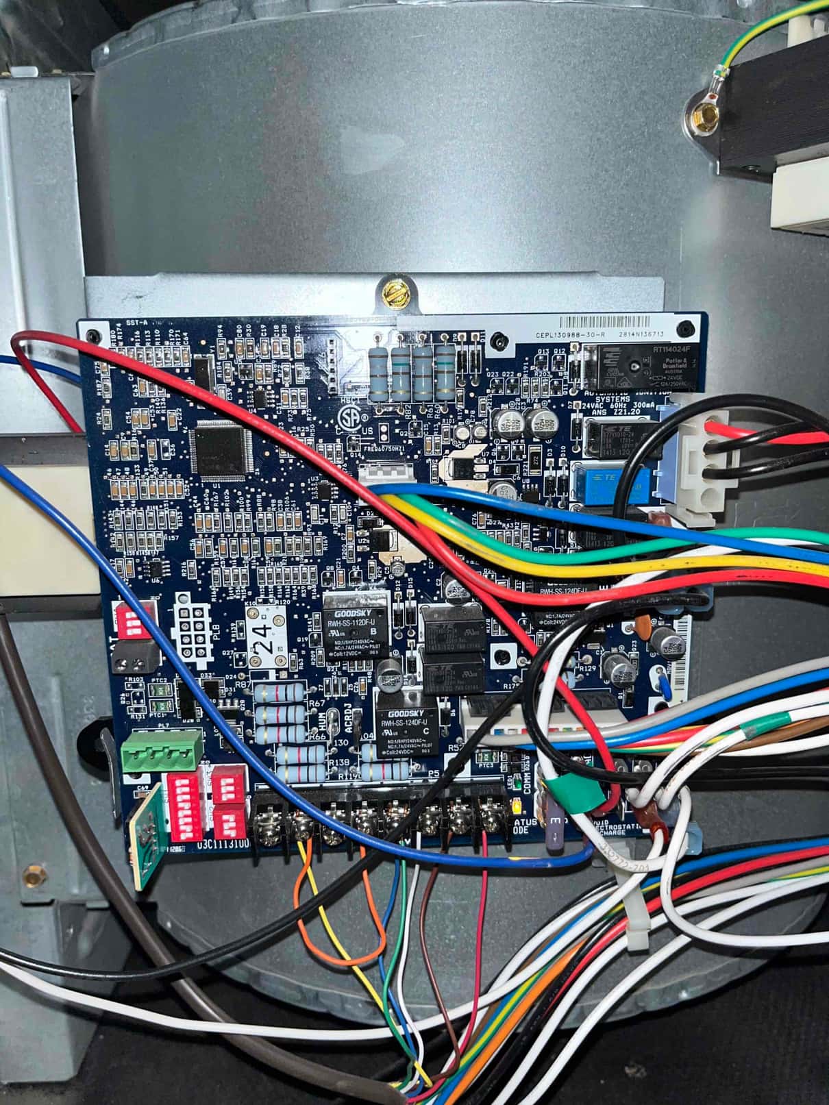 Furnace control board mounted on the blower housing with multiple connected wires, DIP switches, terminal strip, and a bonded ground.