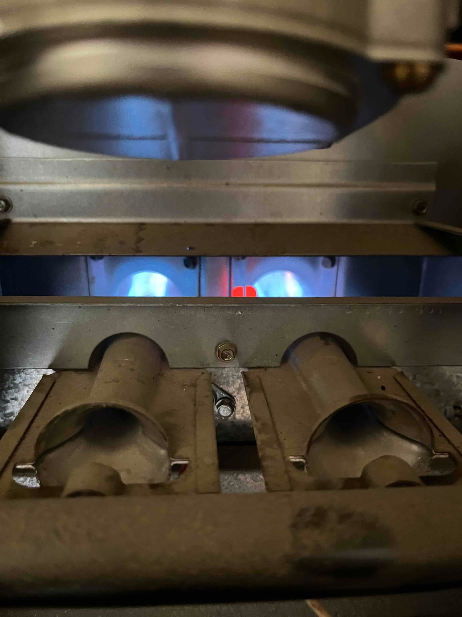 Gas furnace burner compartment with blue flames at two burners and a glowing igniter.