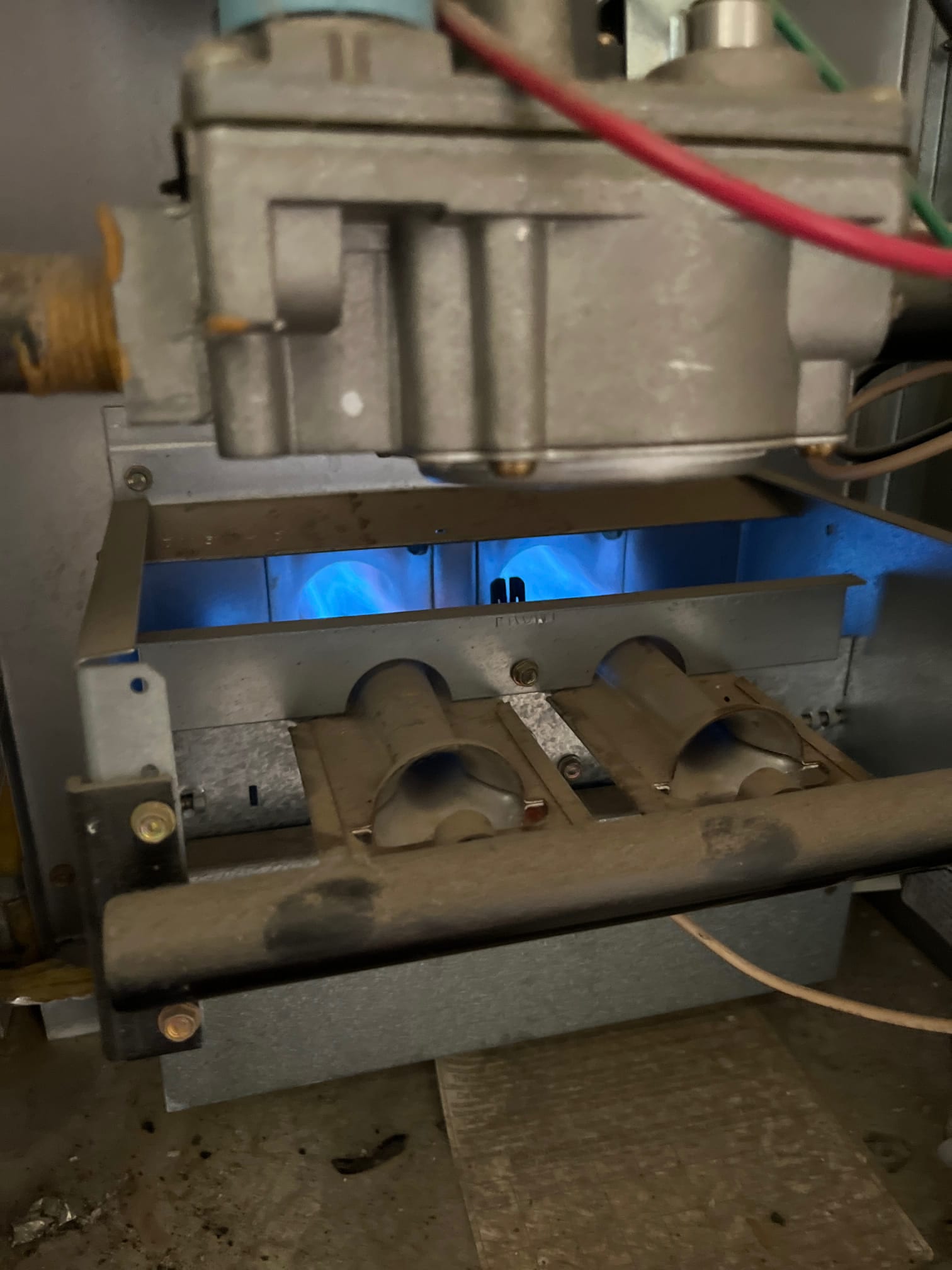 Gas furnace burner compartment shows blue flames at the heat exchanger with dusty burner tubes and manifold.