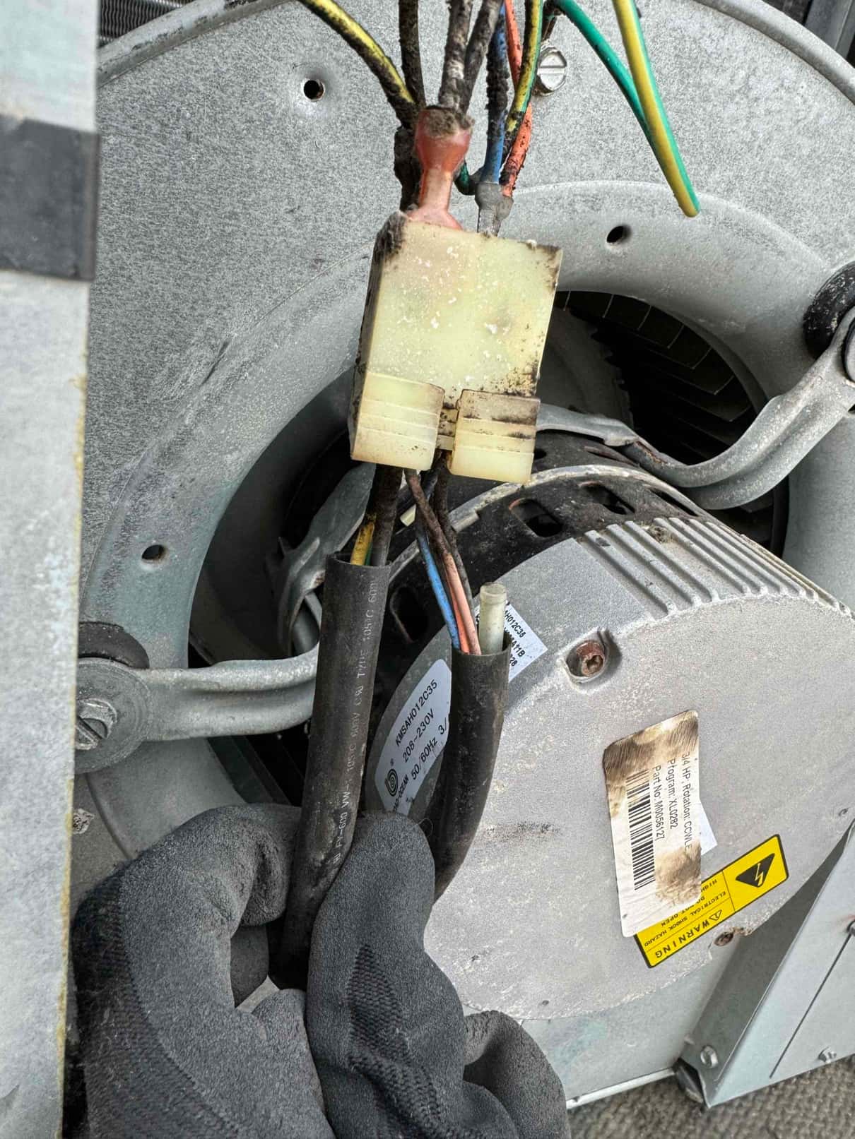 Gloved hand holds wiring harness and plastic connector at a dusty blower motor assembly inside the unit.