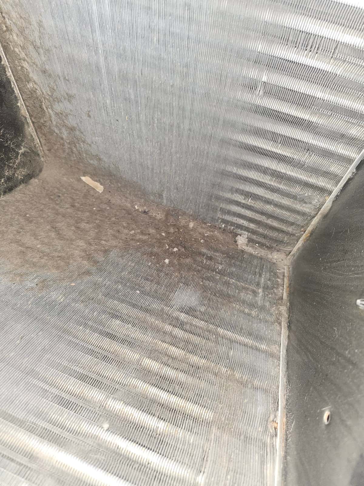 HVAC coil fins and base pan show accumulated dust and debris along the bottom corner of the unit.