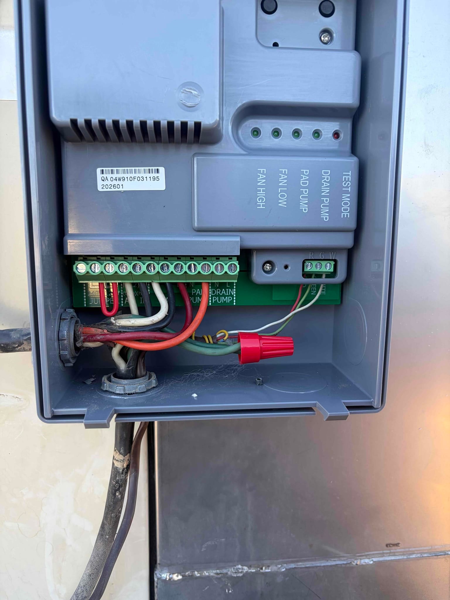 HVAC control box open, showing terminal strip connections, labeled fan and pump indicators, and a red wire nut.