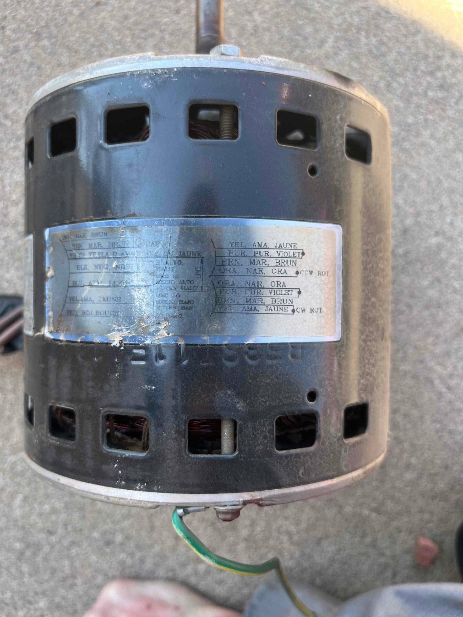 HVAC fan motor removed, housing shows ventilation slots and attached green ground lead; data label visible.