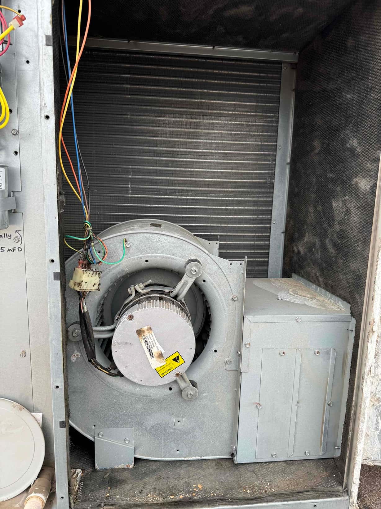 Indoor air handler blower assembly with motor and wiring exposed, with the evaporator coil visible behind the blower housing.