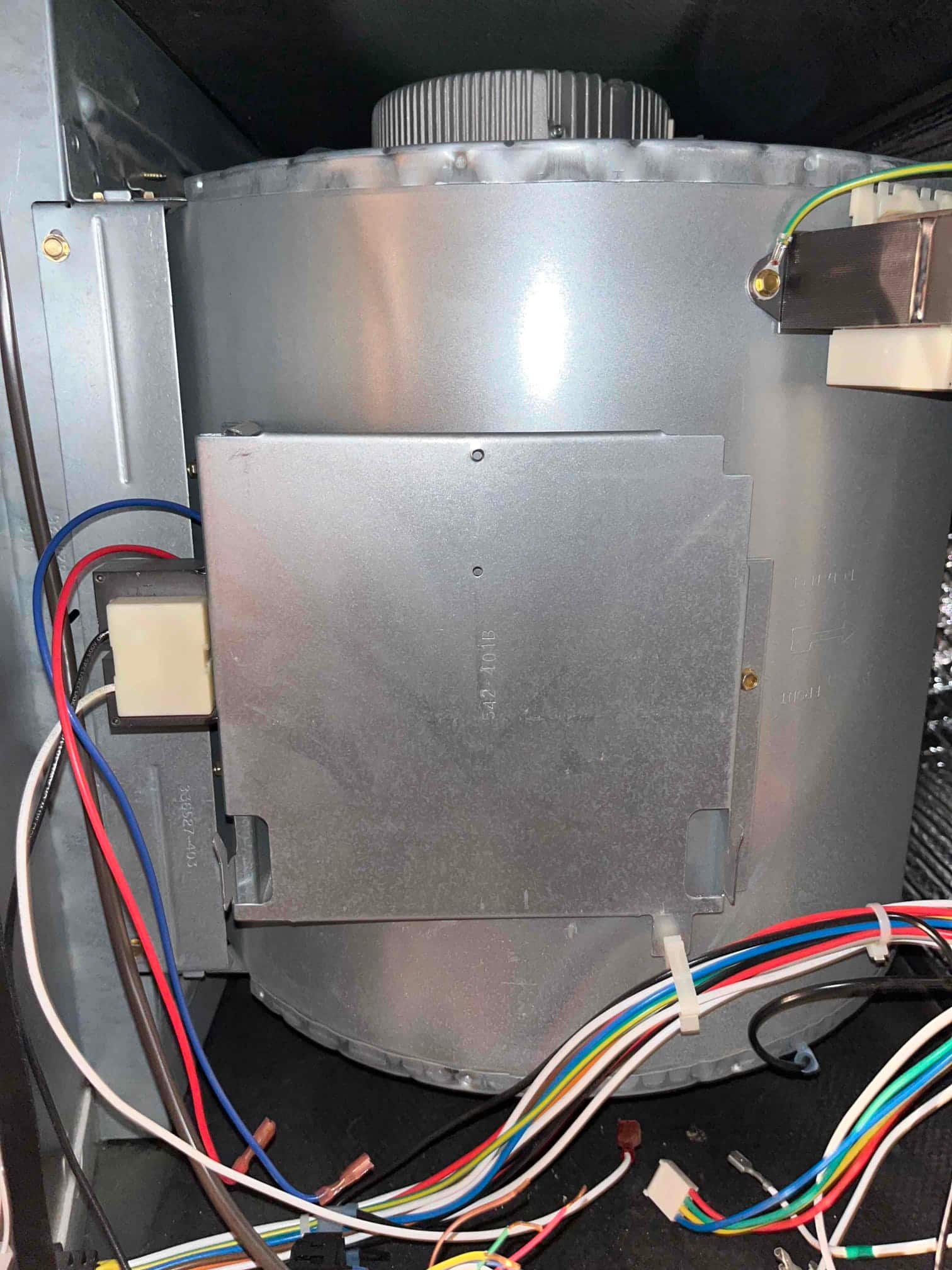 Indoor furnace/air handler blower assembly with metal housing, visible blower wheel, electrical control module cover, and multiple color-coded wiring harnesses.