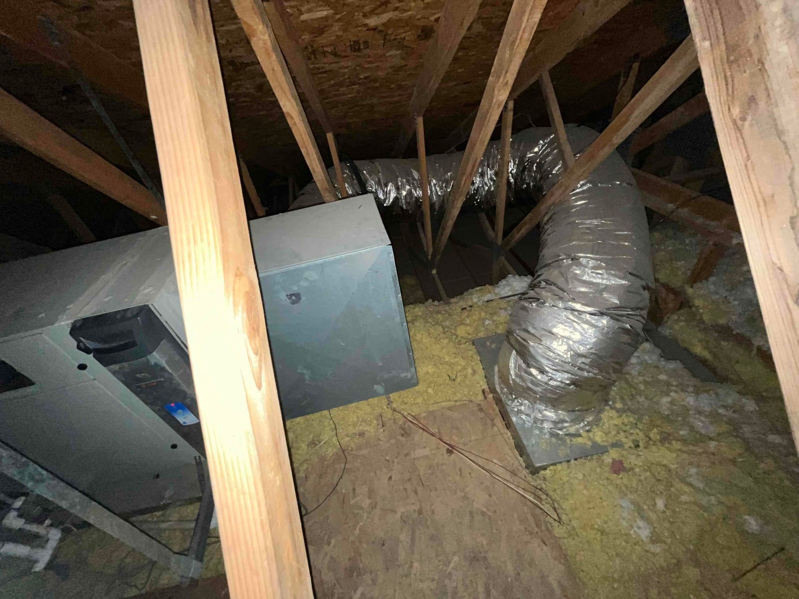 Indoor unit cabinet with insulated flexible duct connected to a sheet-metal plenum amid blown insulation.