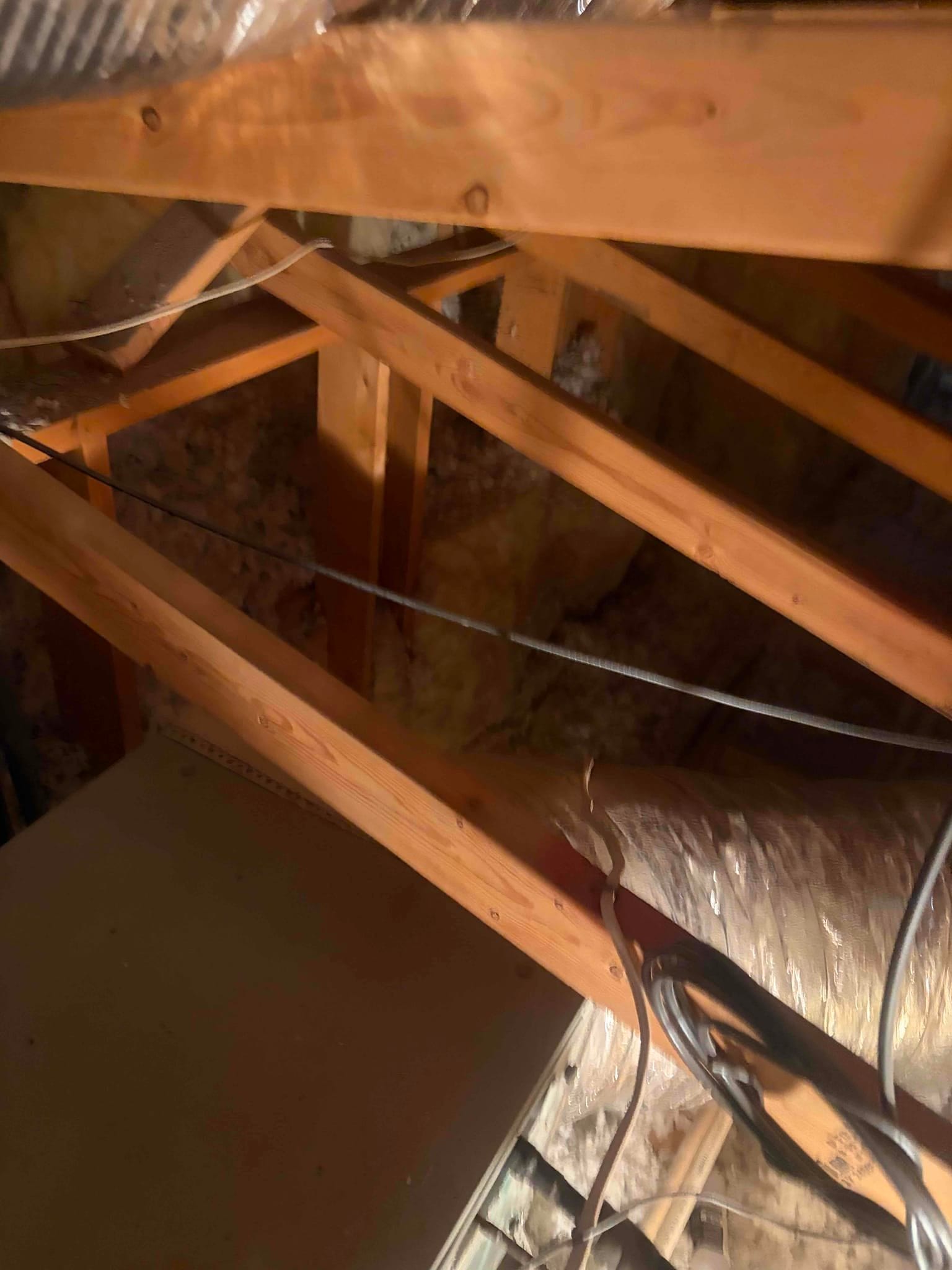 Insulated flexible air duct routed through attic trusses with electrical cables and surrounding insulation.