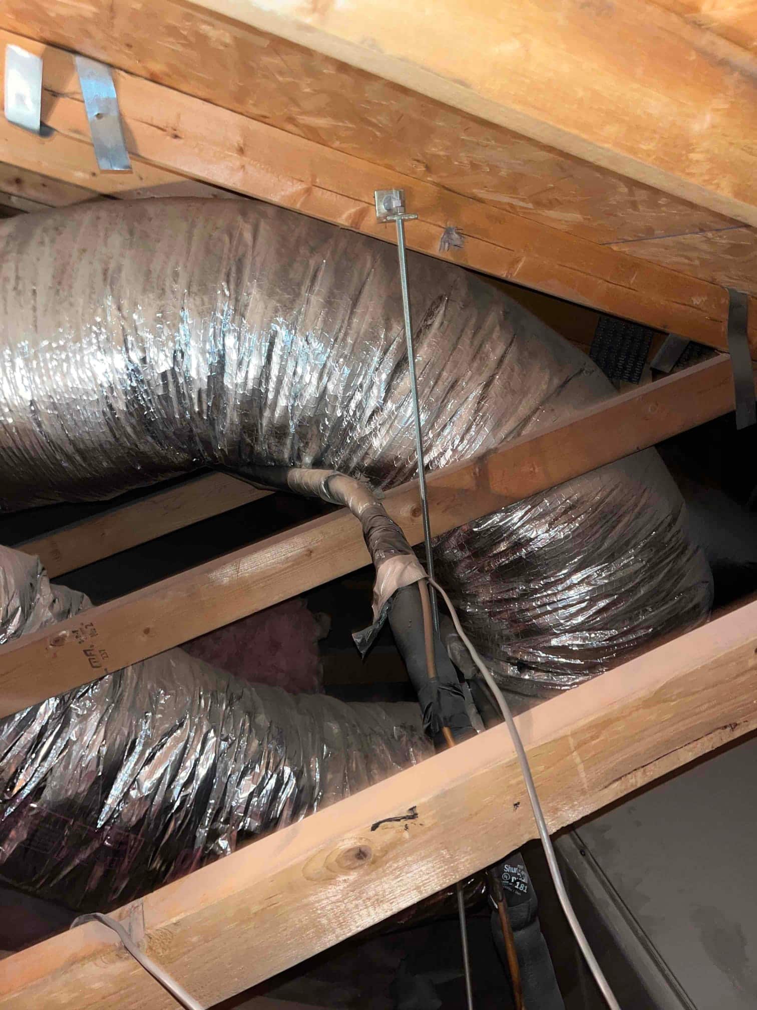 Insulated flexible ducts routed through attic trusses with taped joints and refrigerant lines secured nearby.