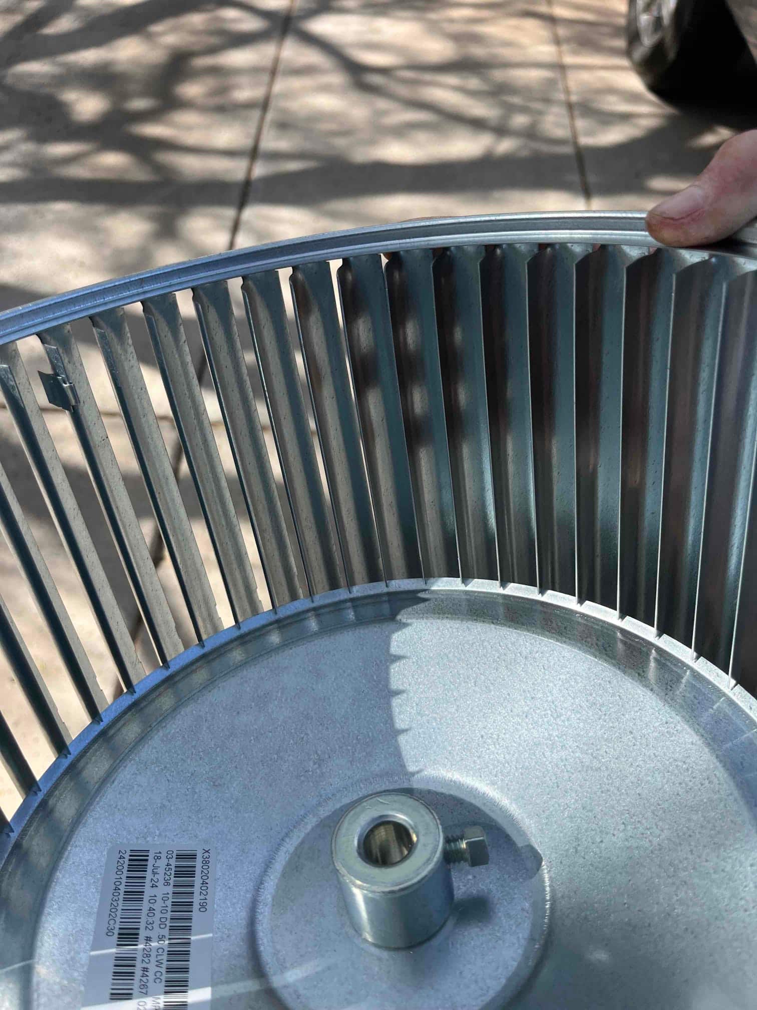 Metal blower wheel with hub and set screw, showing evenly spaced fins and a barcode label on the endplate.
