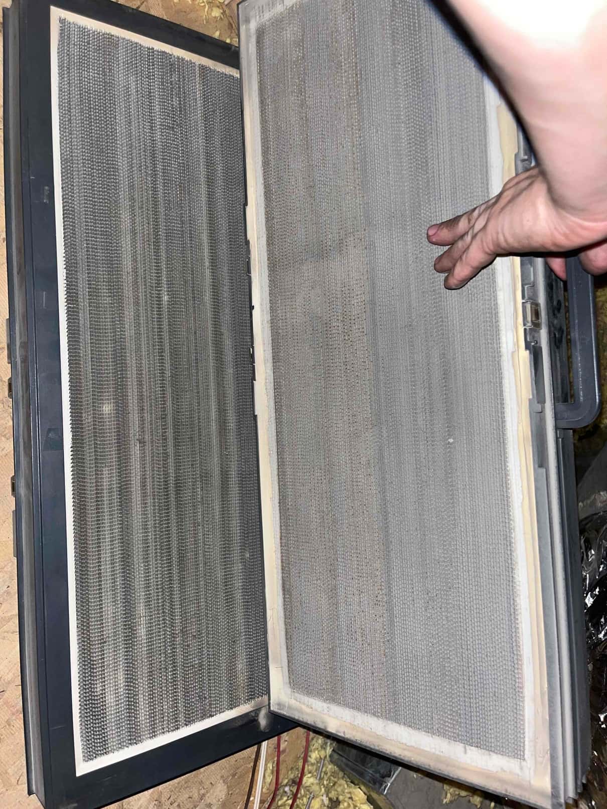 Two metal mesh air filters in a hinged frame are opened for inspection, with a hand holding one side.