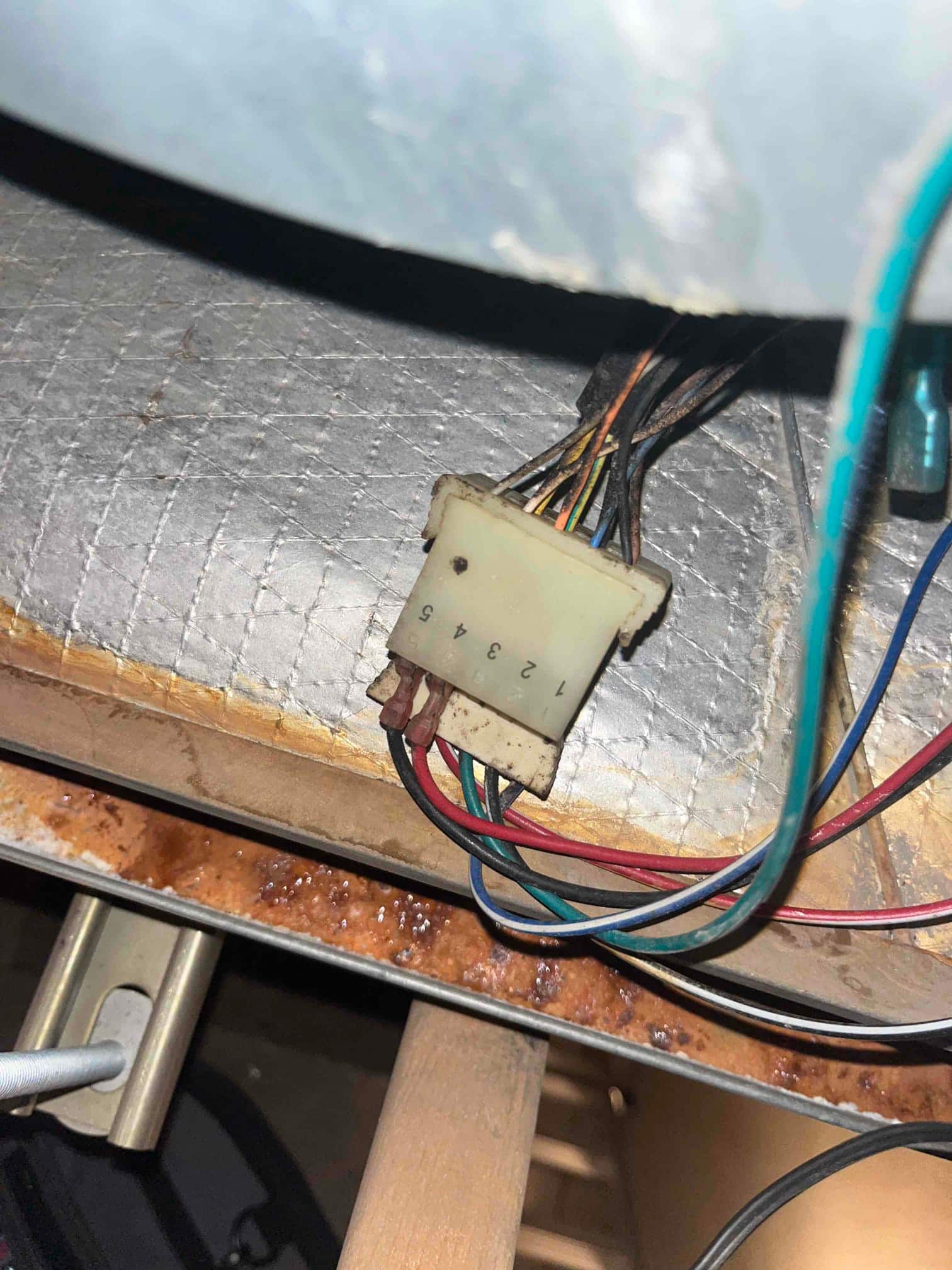 Numbered plastic wiring connector labeled 1–5 with multiple colored wires beside rusted metal surface inside the unit.