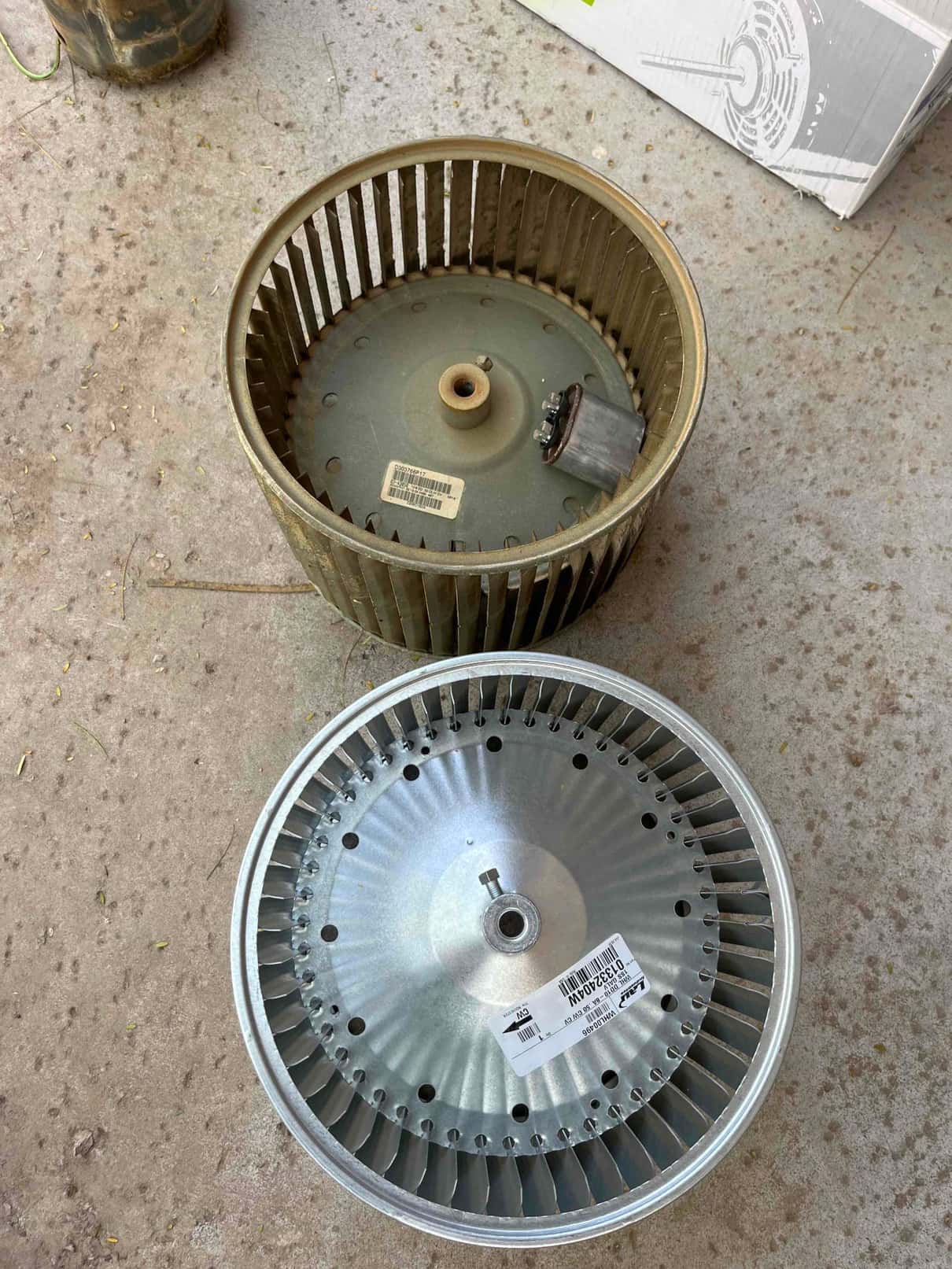 Old blower wheel with dust and corrosion beside a new, clean blower wheel on the floor.
