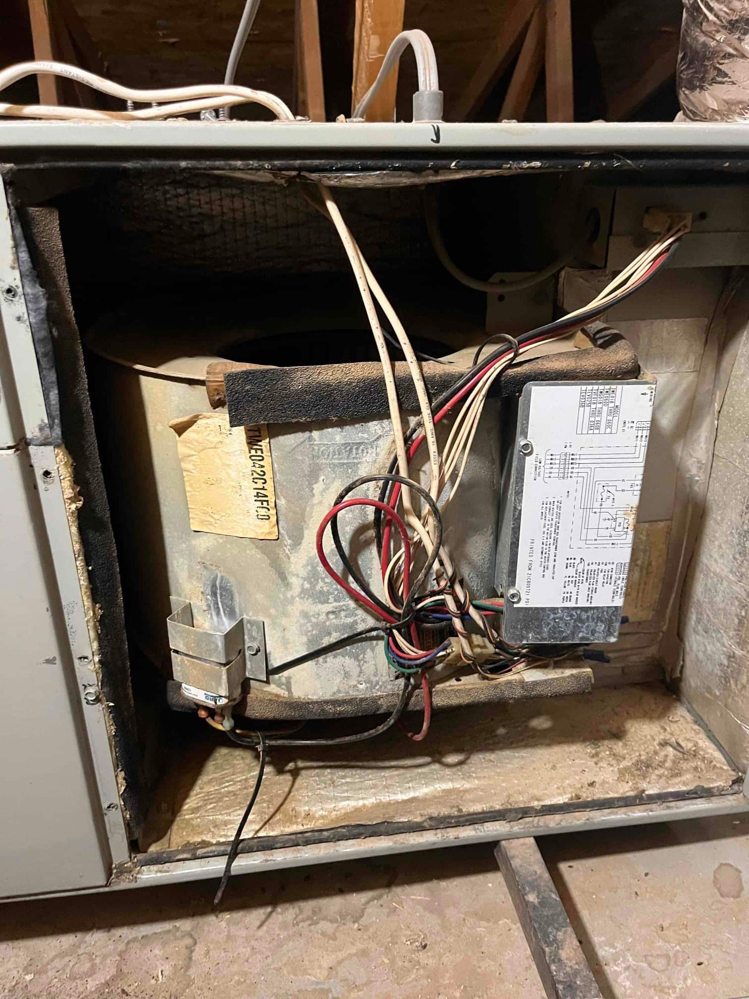 Open air handler cabinet shows the blower housing, control module with wiring harness, condensate drain tubing, and accumulated dust.