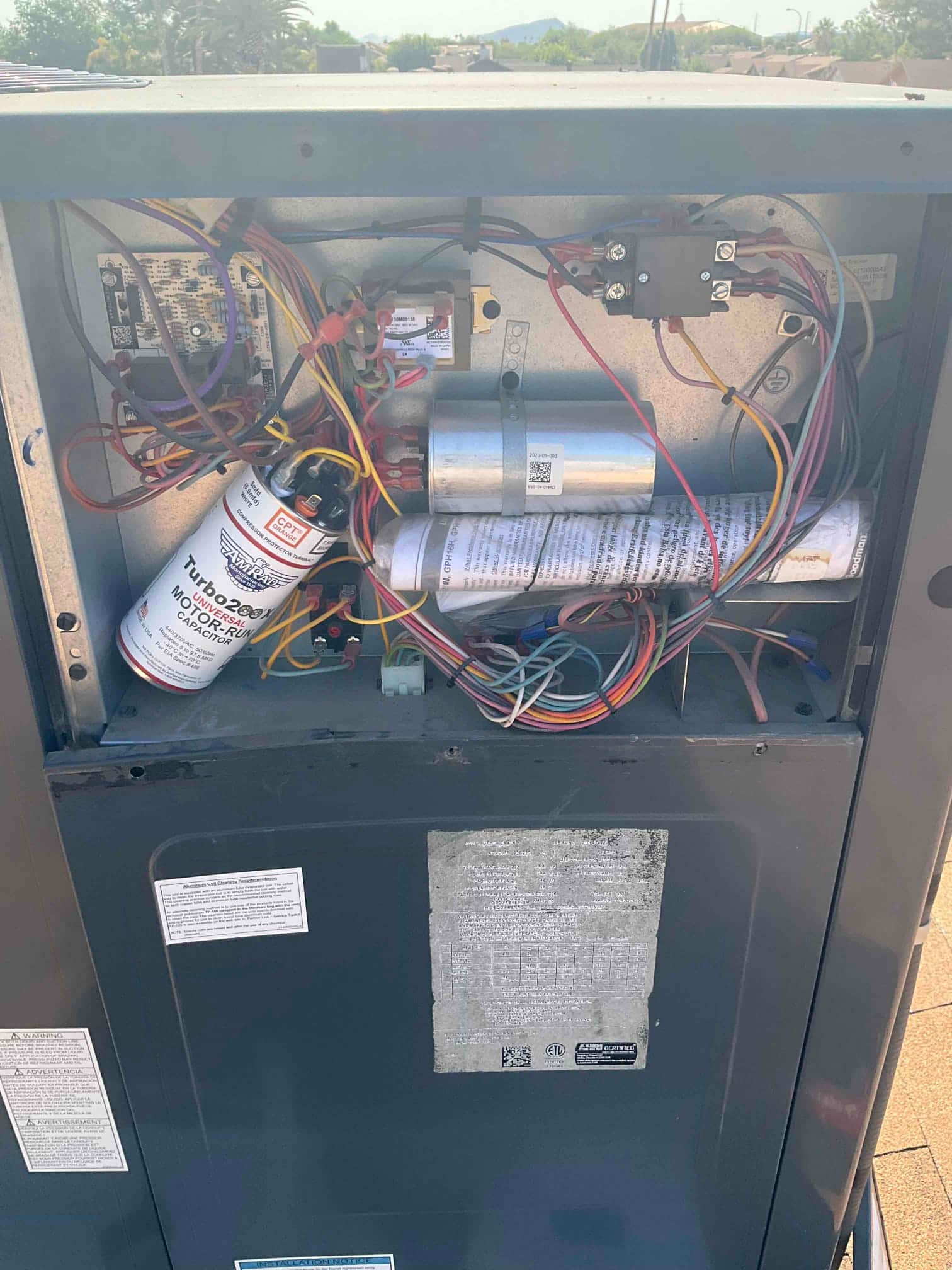 Open condenser control compartment showing two capacitors, contactor, transformer, control board, and connected wiring.