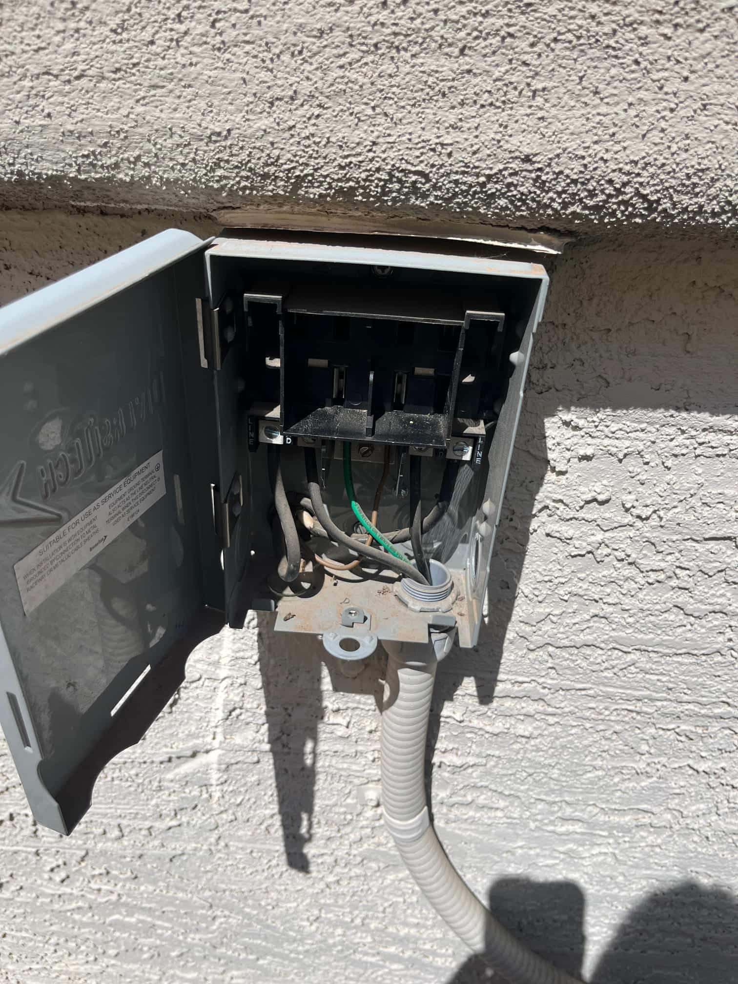 Outdoor air conditioner disconnect box open, showing line and load conductors, ground wire, and flexible conduit.