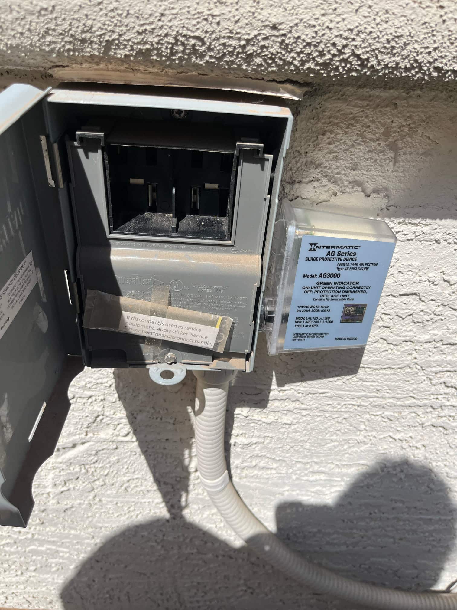 Outdoor air conditioner disconnect box open with pull-out handle compartment visible, alongside a surge protective device and flexible conduit.