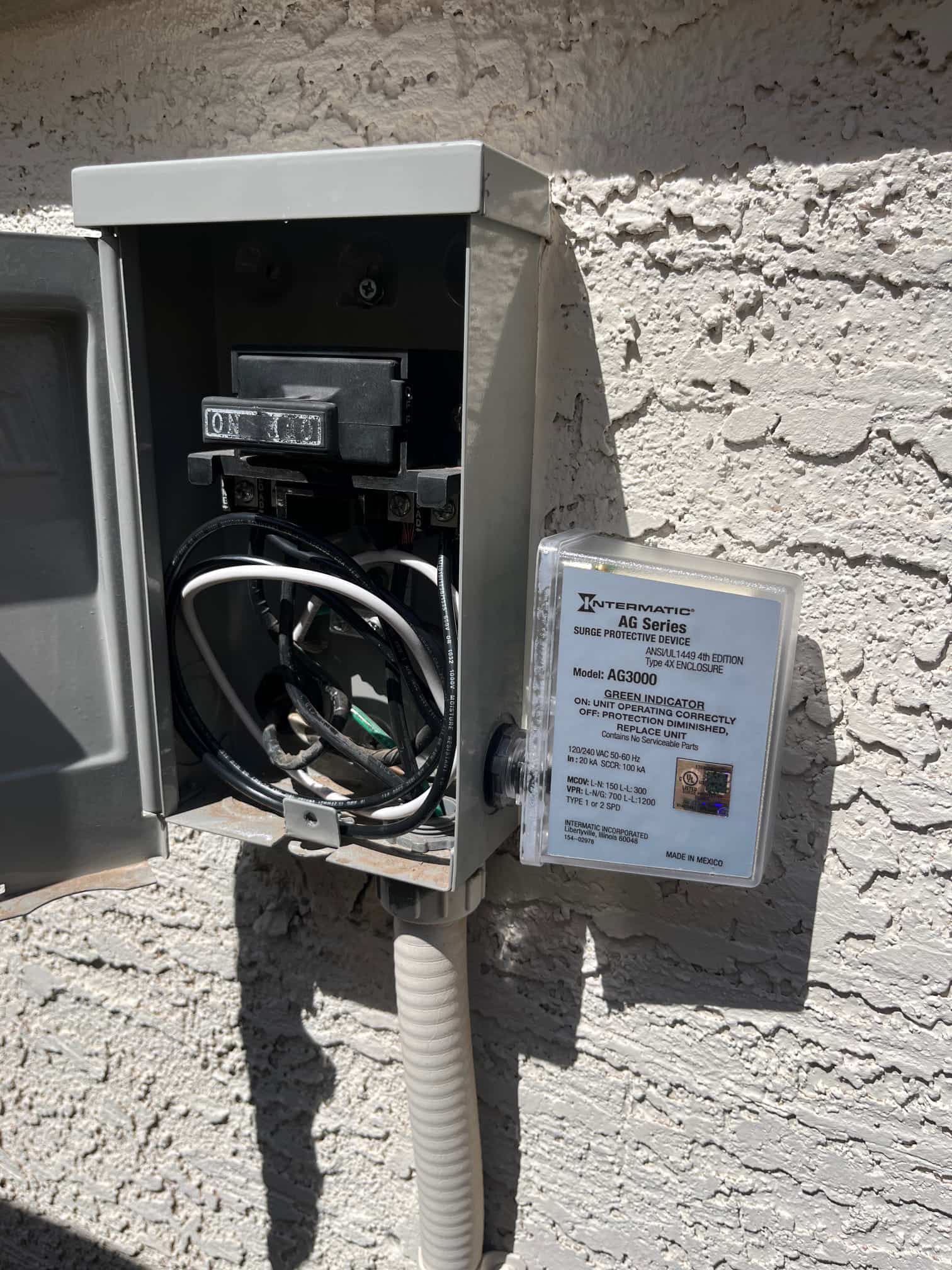 Outdoor air conditioner disconnect box open, showing pull-out ON/OFF handle, internal wiring, and an attached surge protective device.