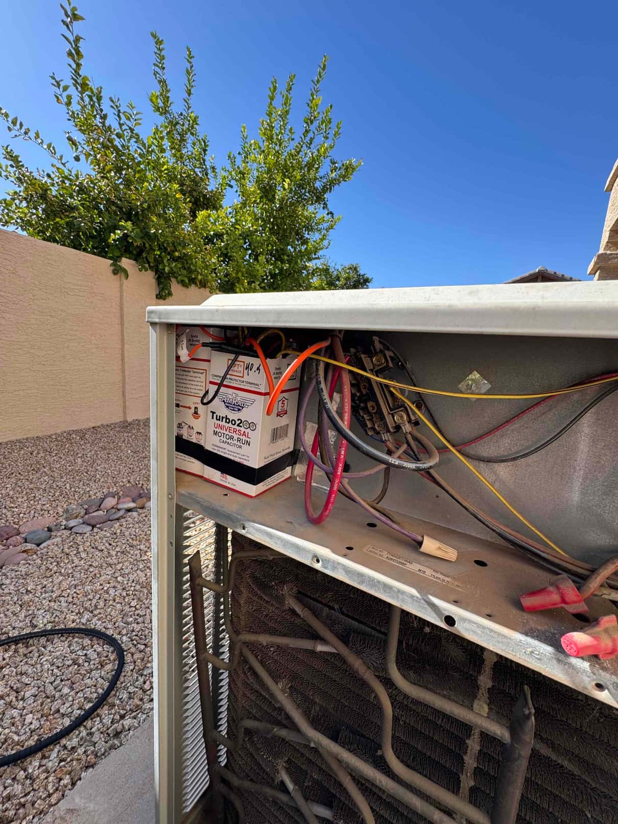 Outdoor condenser cabinet open, showing control wiring, contactor, coil, and a boxed motor-run capacitor.